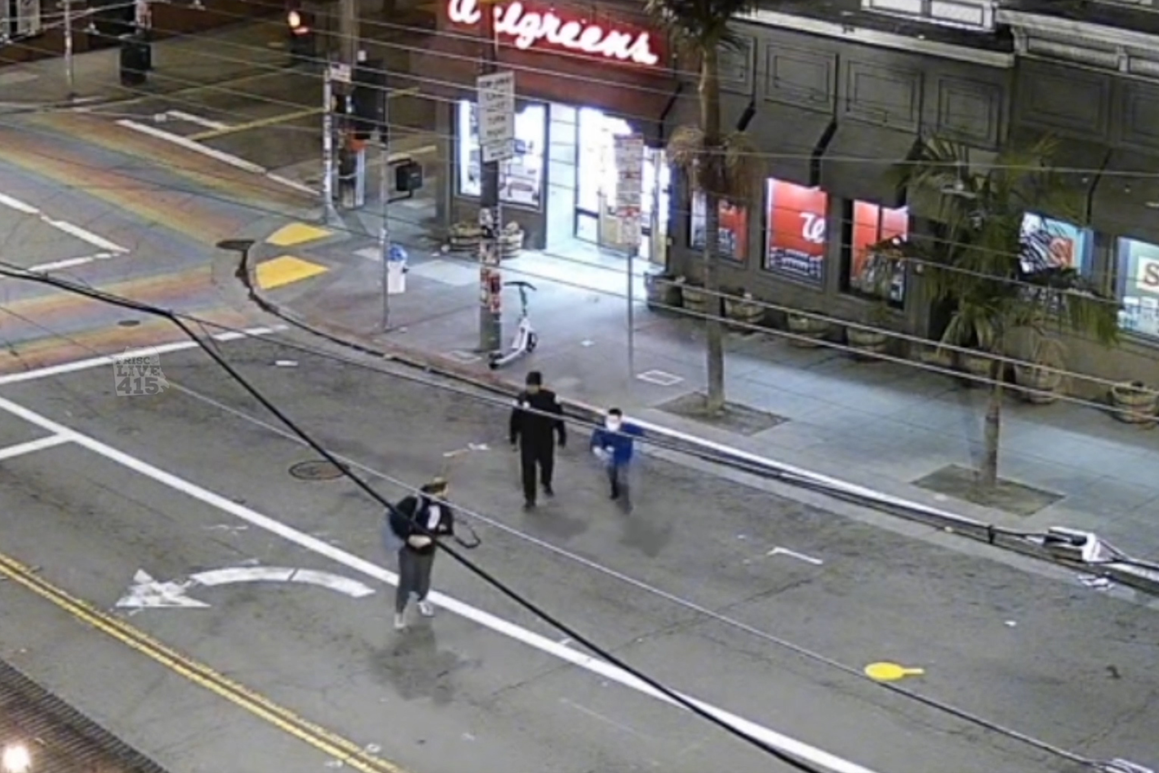 Three people are seen on a quiet city street at night. A brightly lit store is in the background, with palm trees lining the sidewalk.