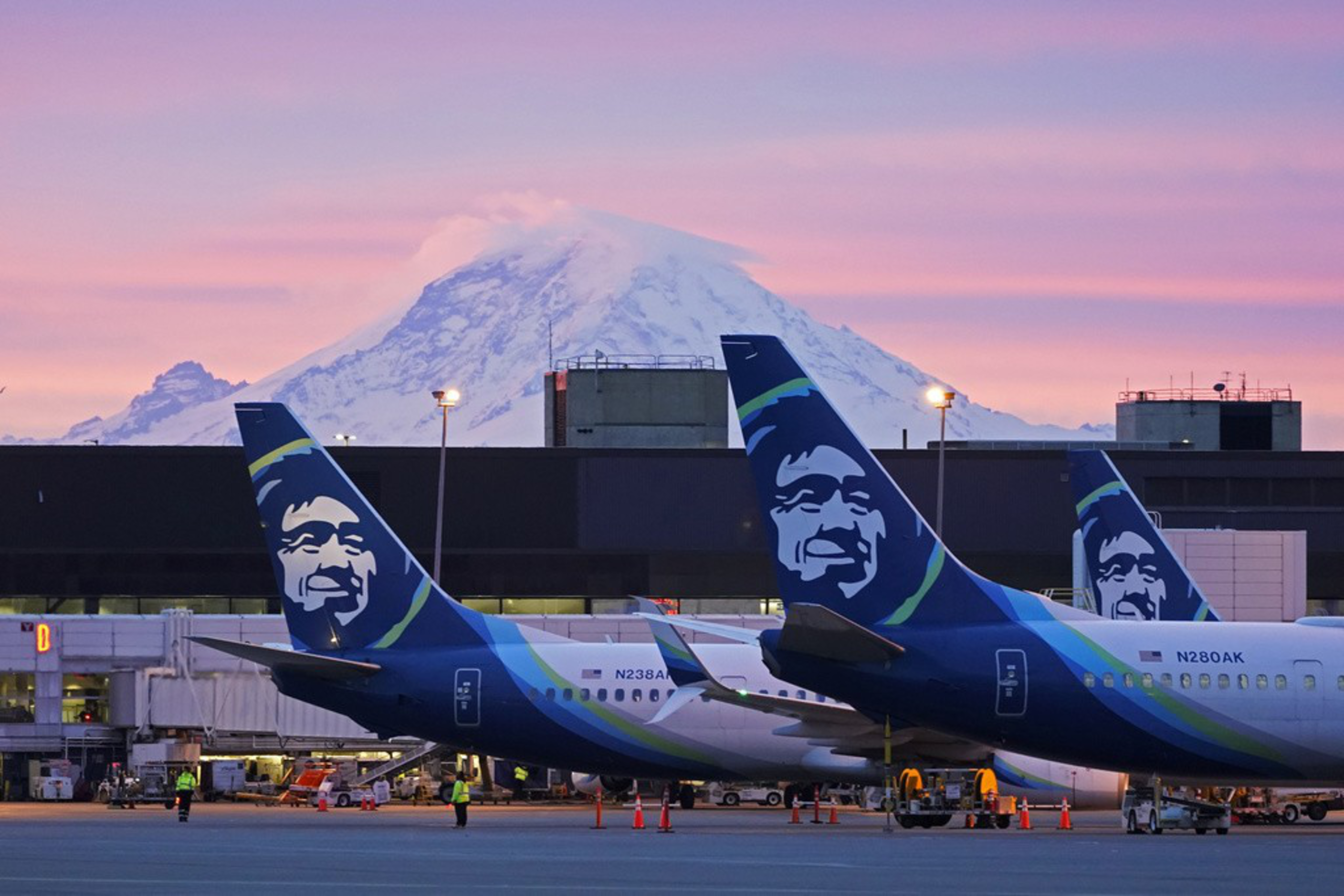 Two airplanes parked on a runway with mountains in the background.