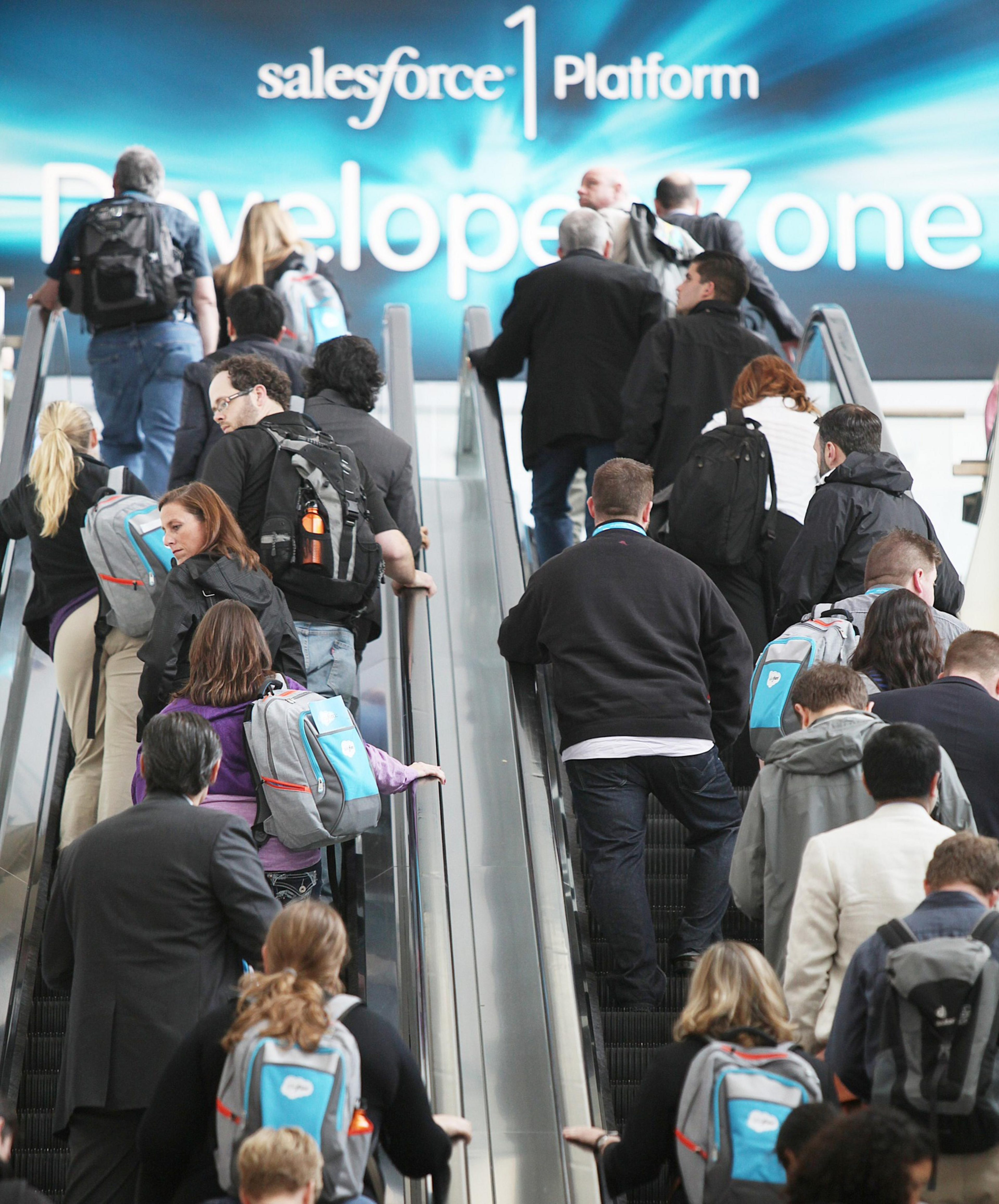 People make their way up an escalator with Salesforce signage in the background