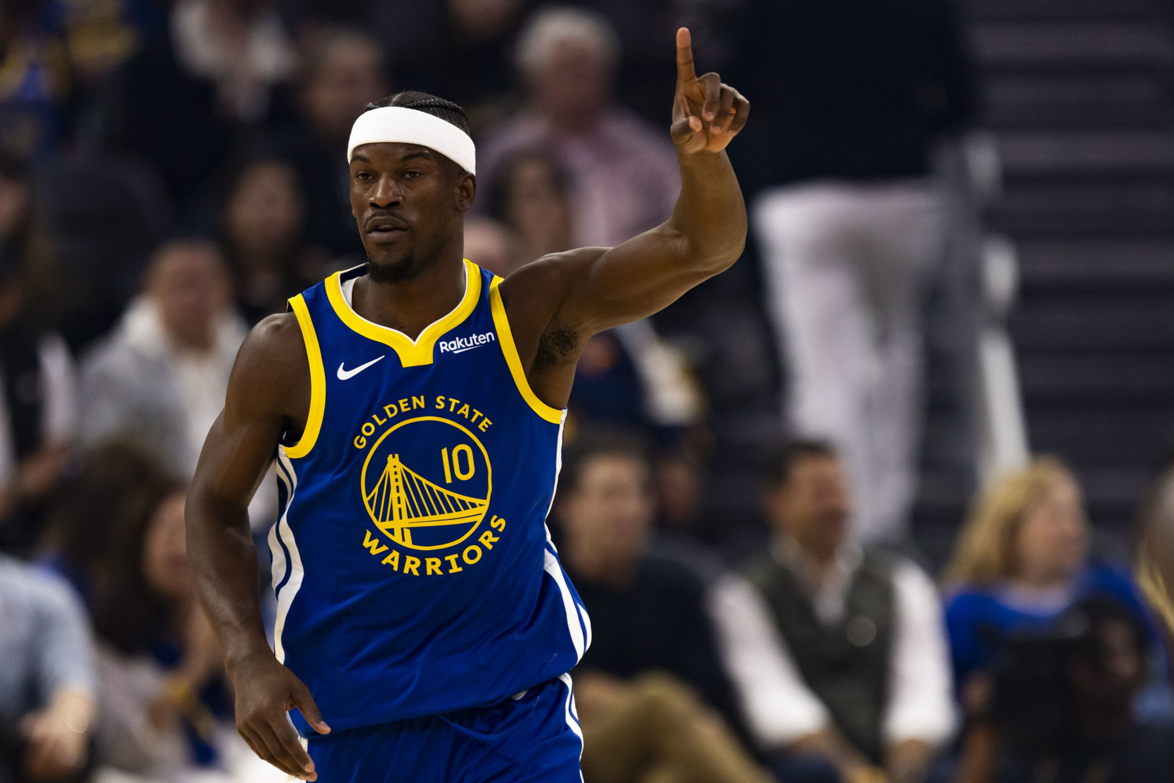 A Golden State Warriors basketball player wearing jersey number 10 raises his right arm with his index finger pointing up during a game.