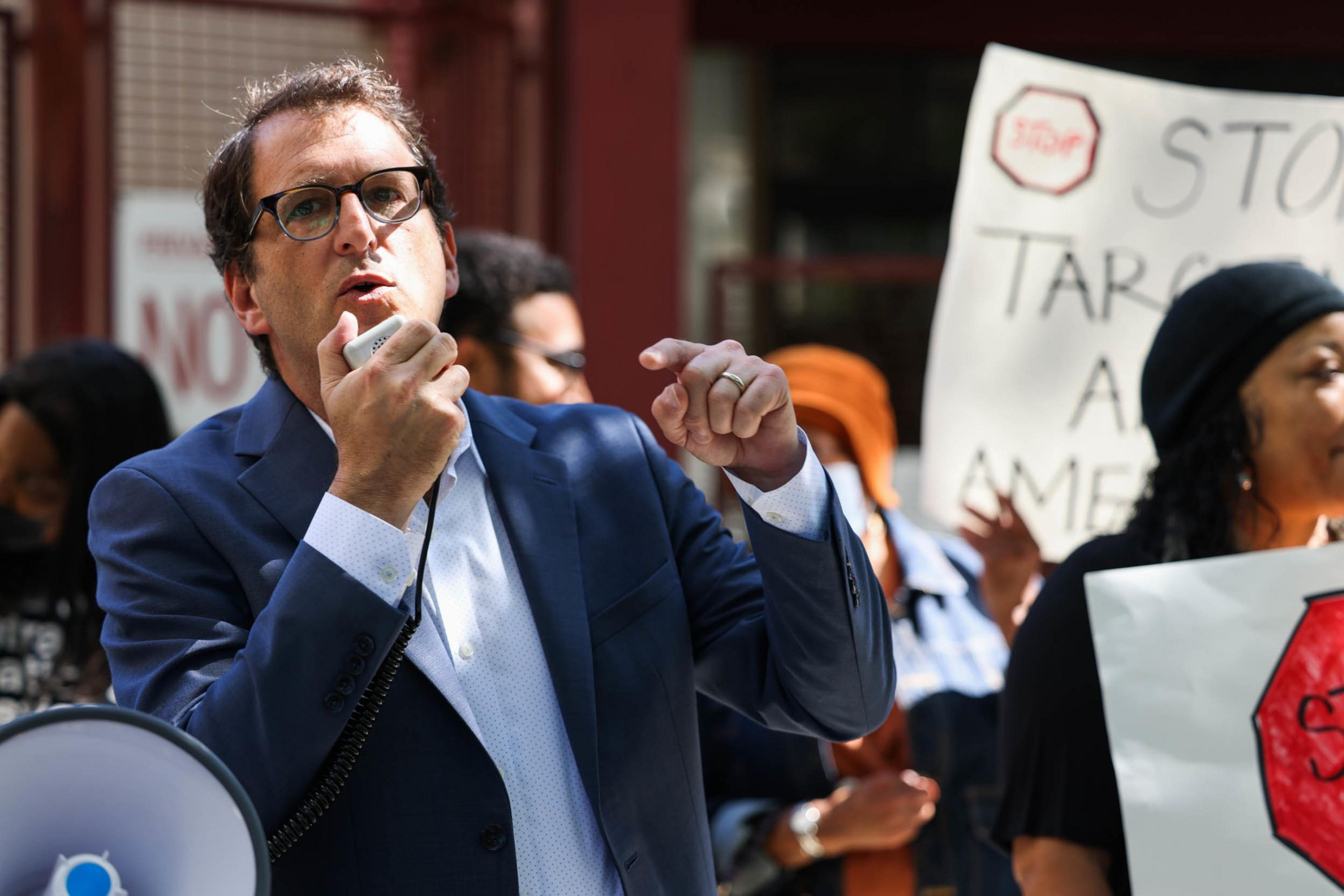 A man in a blue suit speaks at an outdoor rally