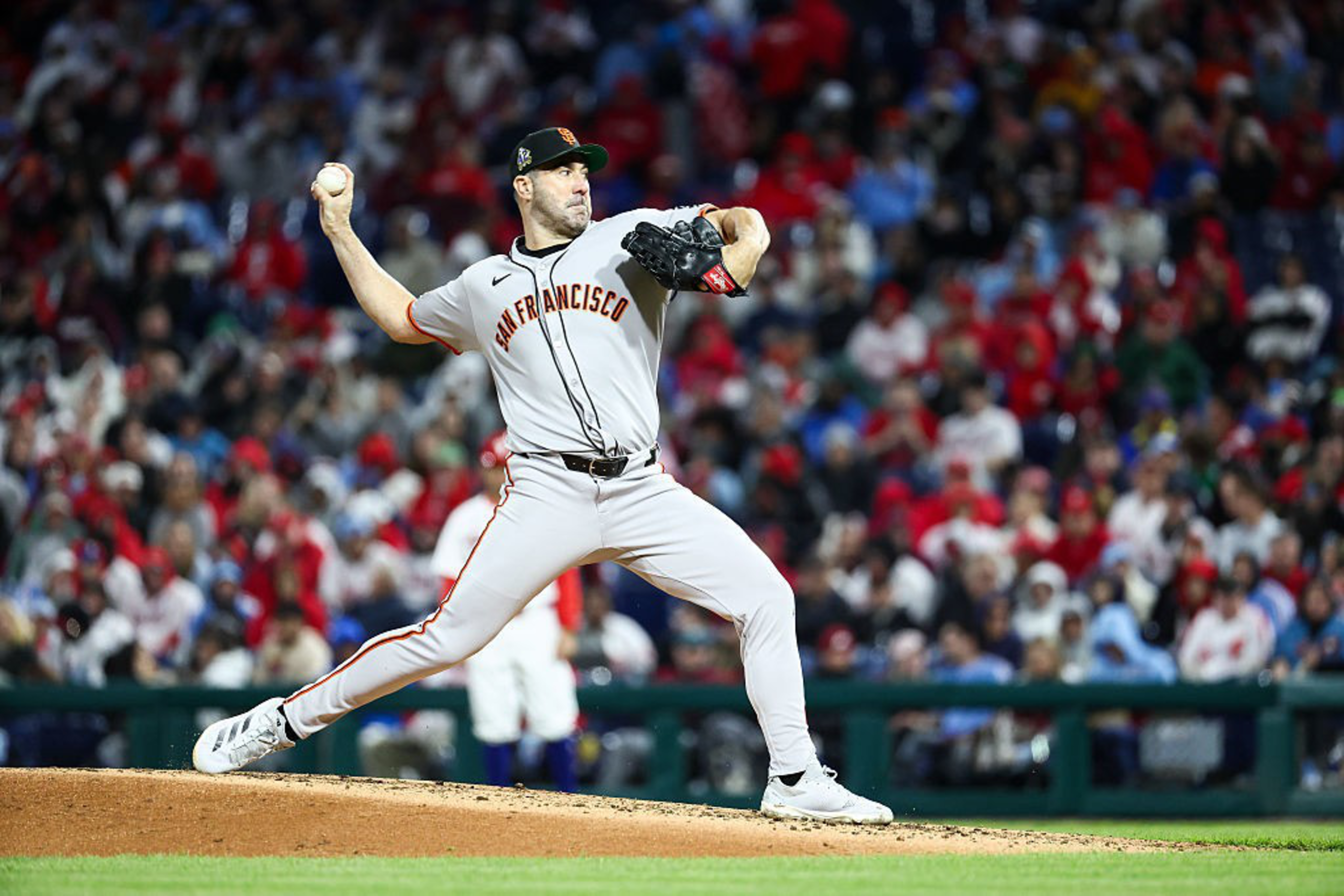 A baseball player in a San Francisco Giants uniform is pitching on a mound, surrounded by a blurred crowd in a stadium.