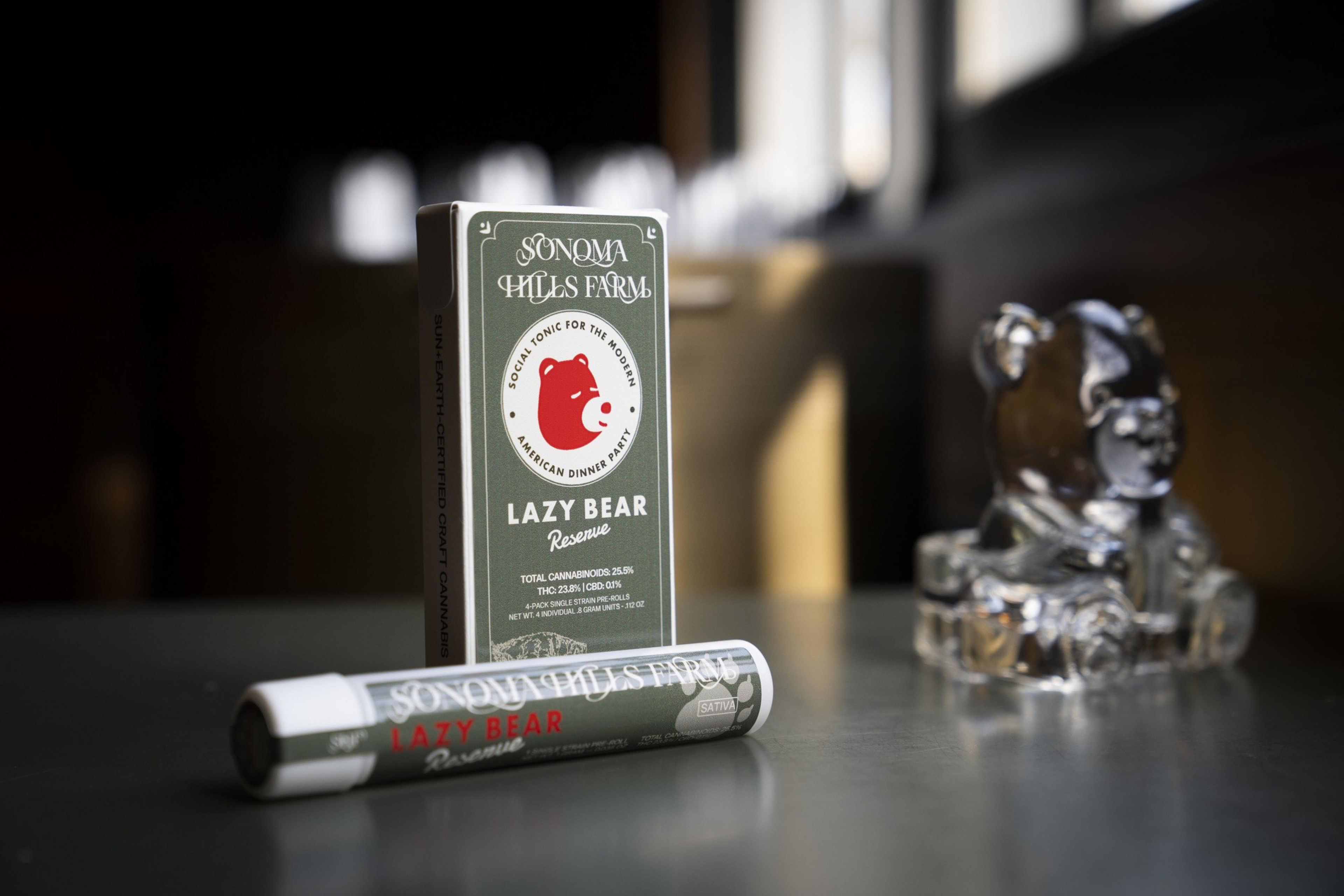 A cannabis product package labeled &quot;Lazy Bear Reserve&quot; from Sonoma Hills Farm stands on a table, alongside a glass bear figurine.