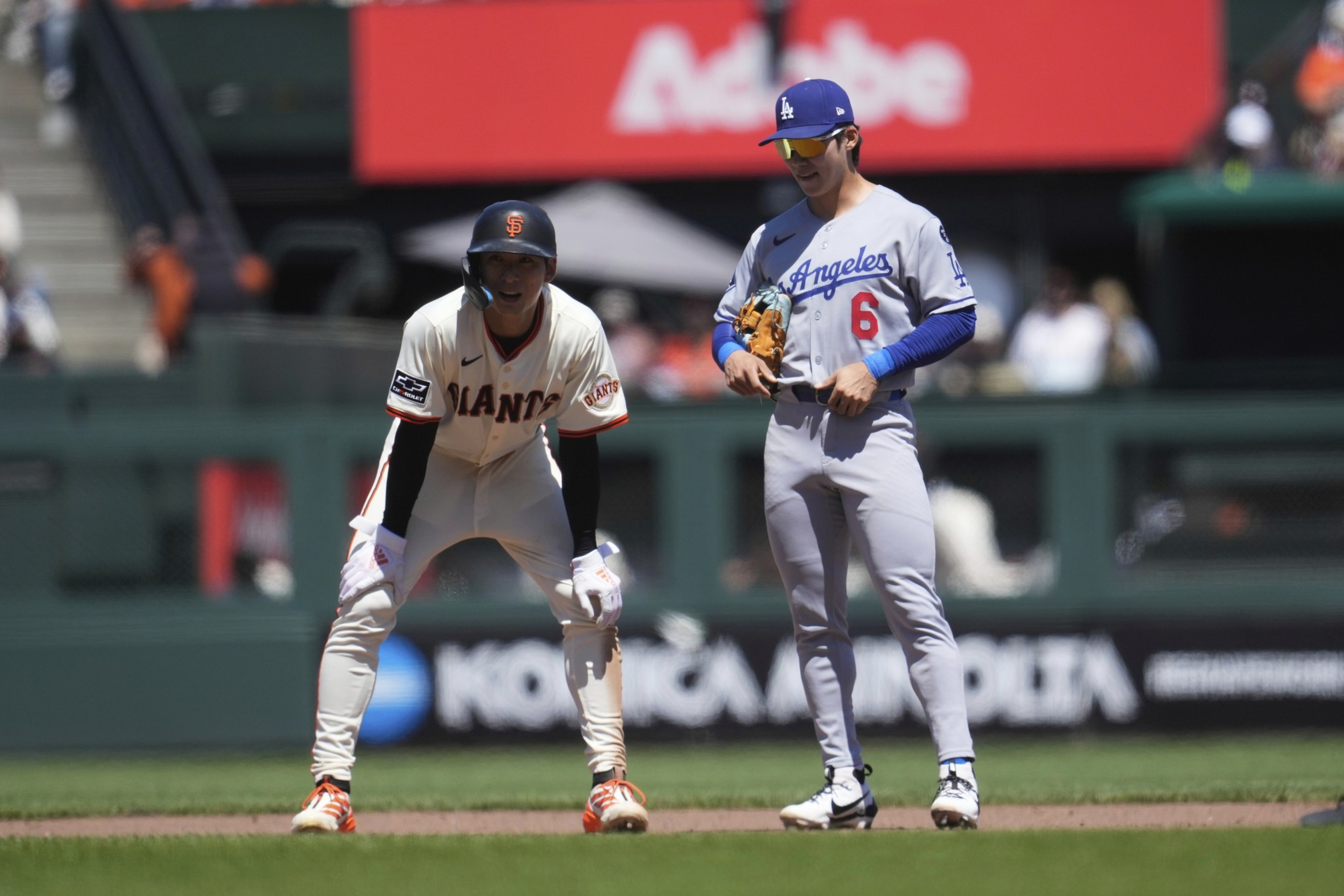 In the image, two baseball players stand on the field. One wears an orange jersey with &quot;Giants,&quot; the other a blue jersey with &quot;Angeles.&quot; They appear focused on the game.