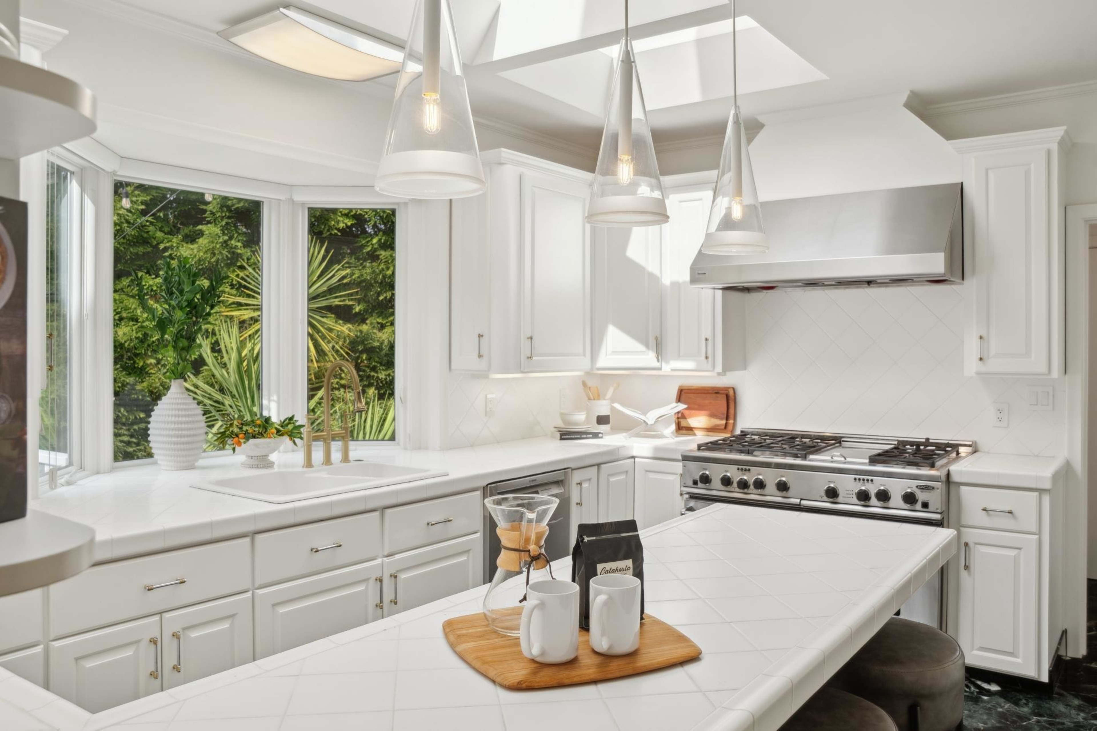 A bright kitchen with white cabinets, a gas stove, and a large island featuring a coffee setup and pendant lighting above.