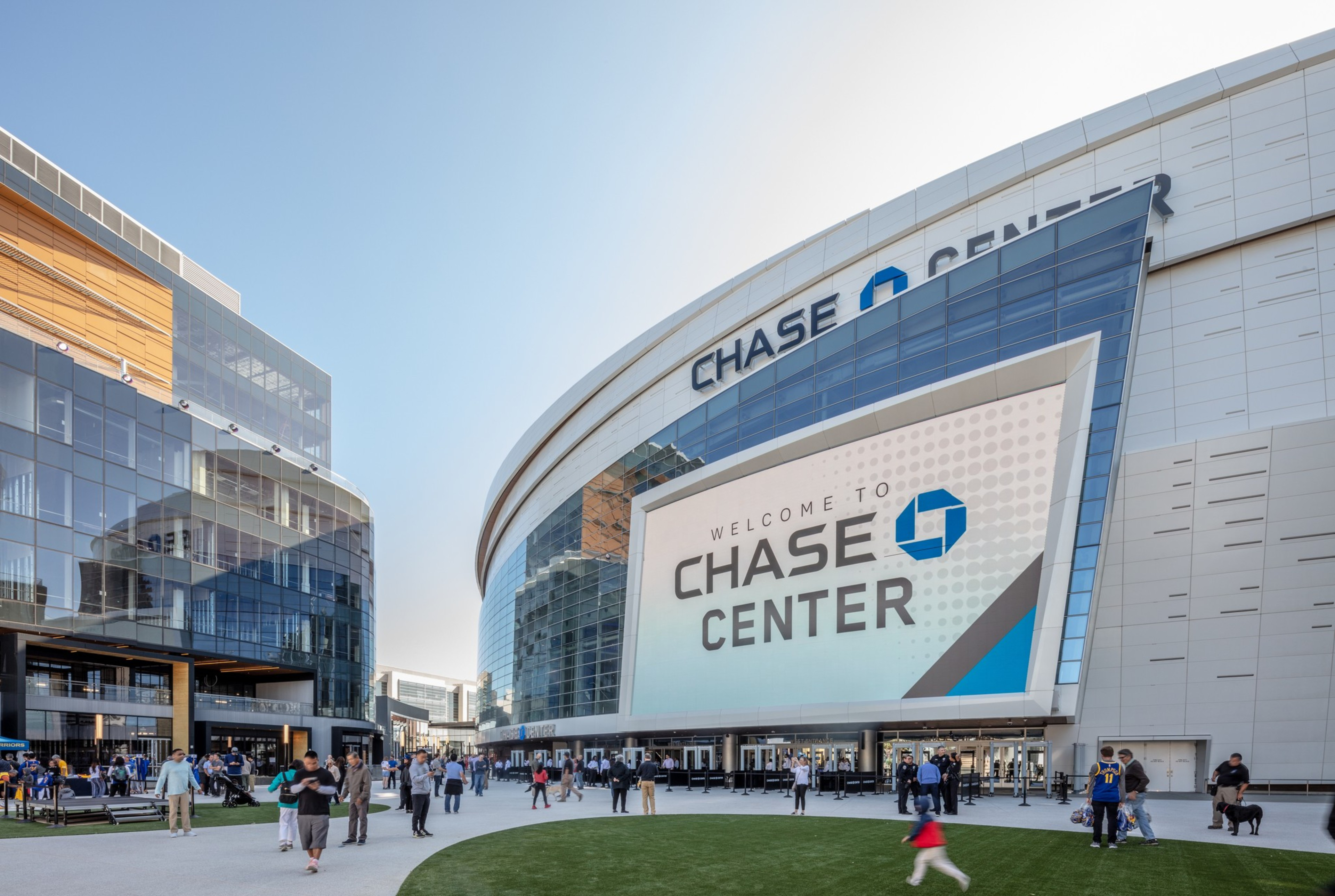 People mill about a plaza and grassy area at Chase Center's Thrive City in San Francisco.