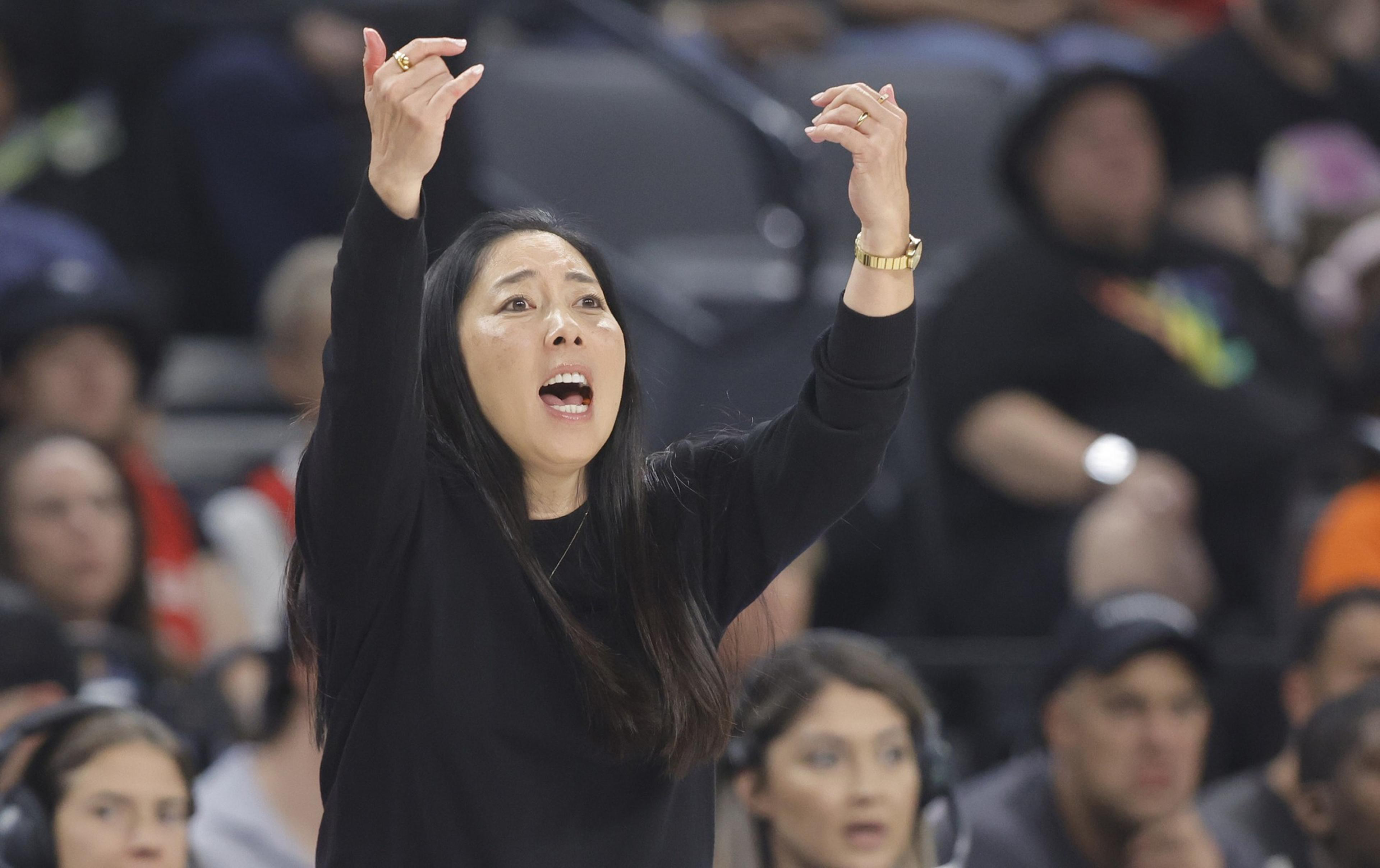 A person wearing a black outfit gestures passionately with raised arms. They appear engaged and animated with an intense expression, in a crowded indoor setting.