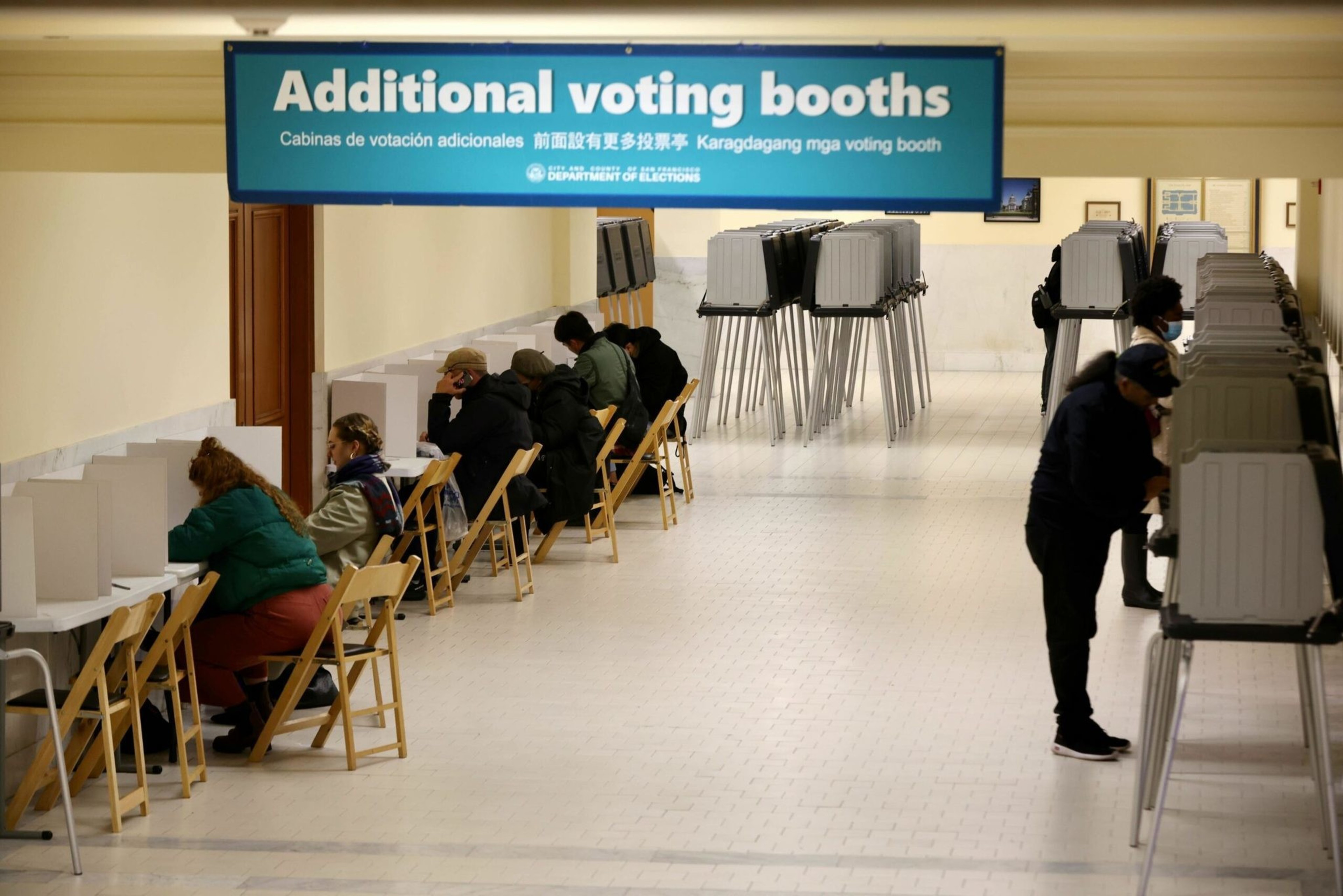 People are voting in booths under a sign reading &quot;Additional voting booths&quot; in various languages.