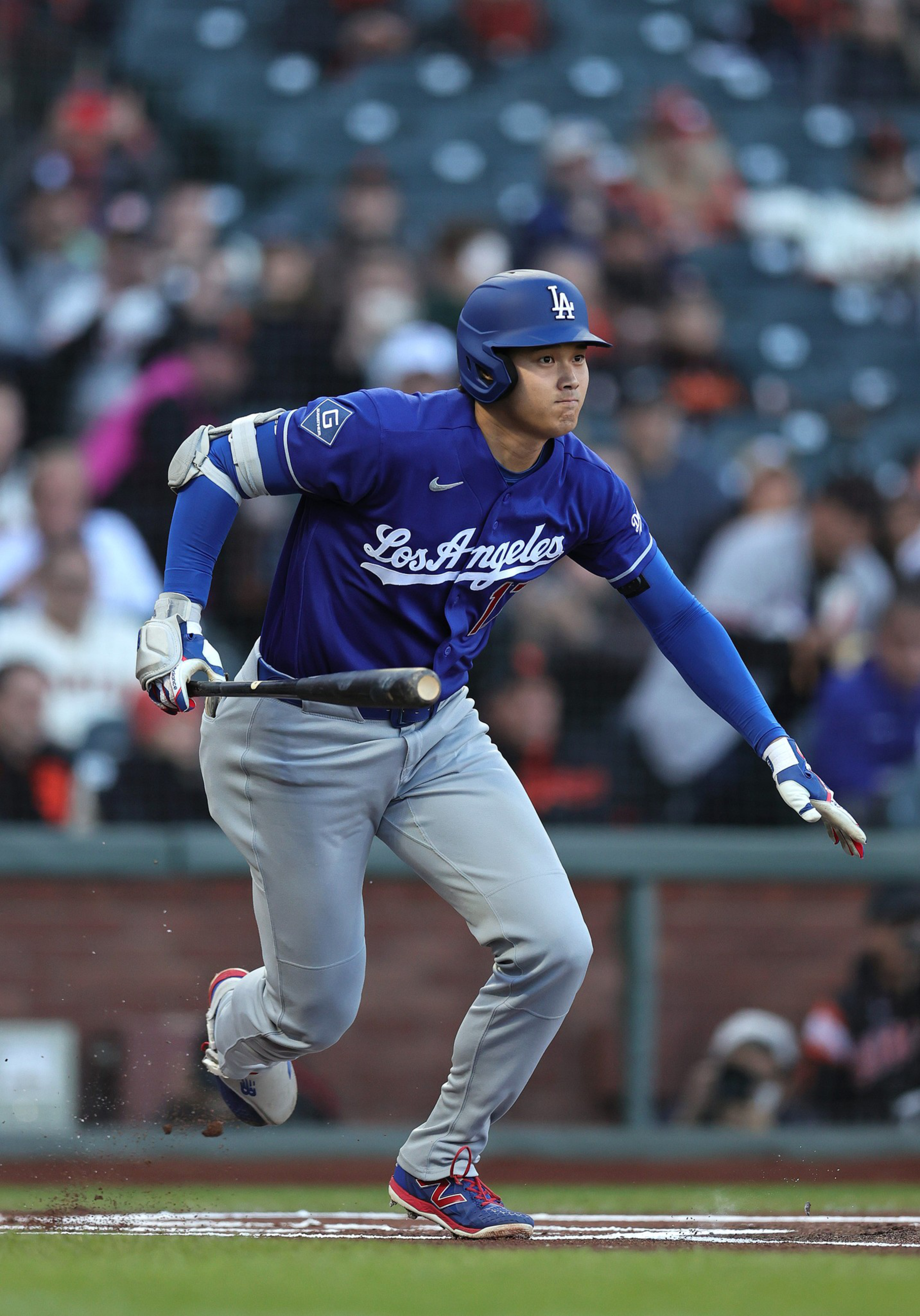 A baseball player in a blue Los Angeles uniform is running, holding a bat, having just hit the ball during a game.