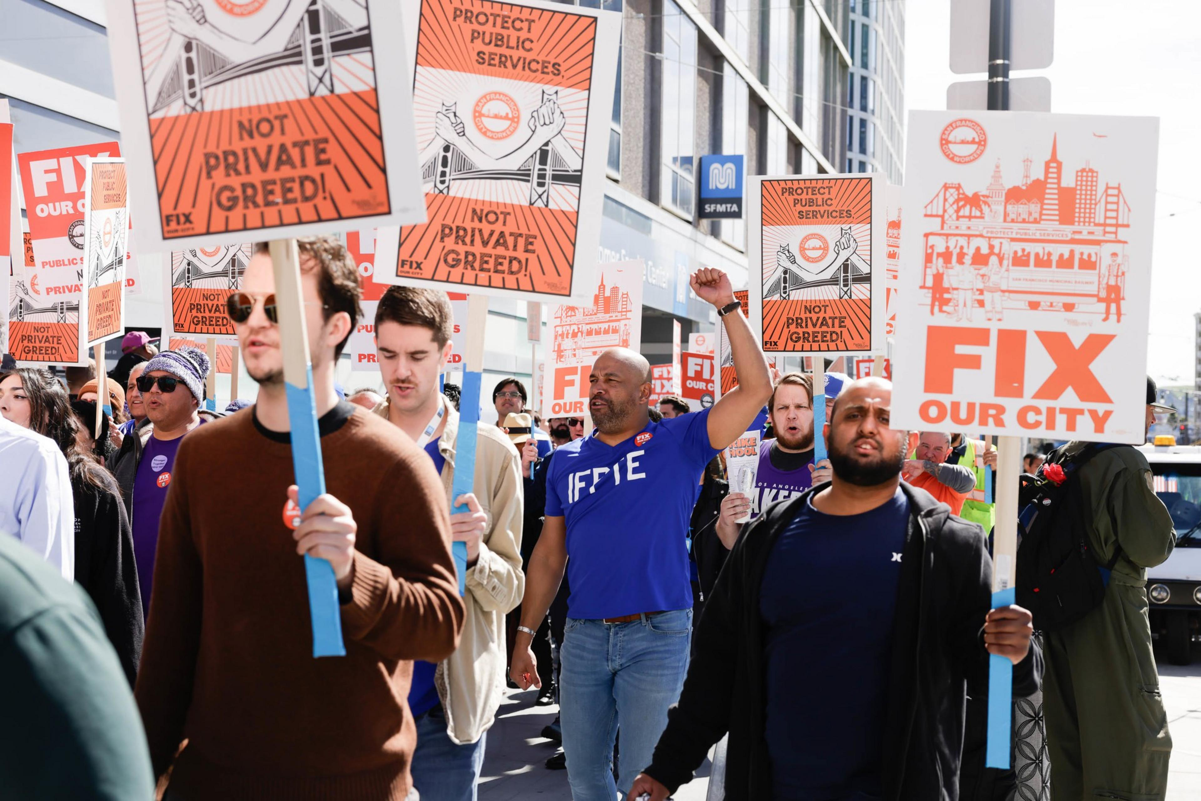 A crowd is marching with signs saying &quot;FIX OUR CITY&quot; and &quot;NOT PRIVATE GREED,&quot; advocating for public services.