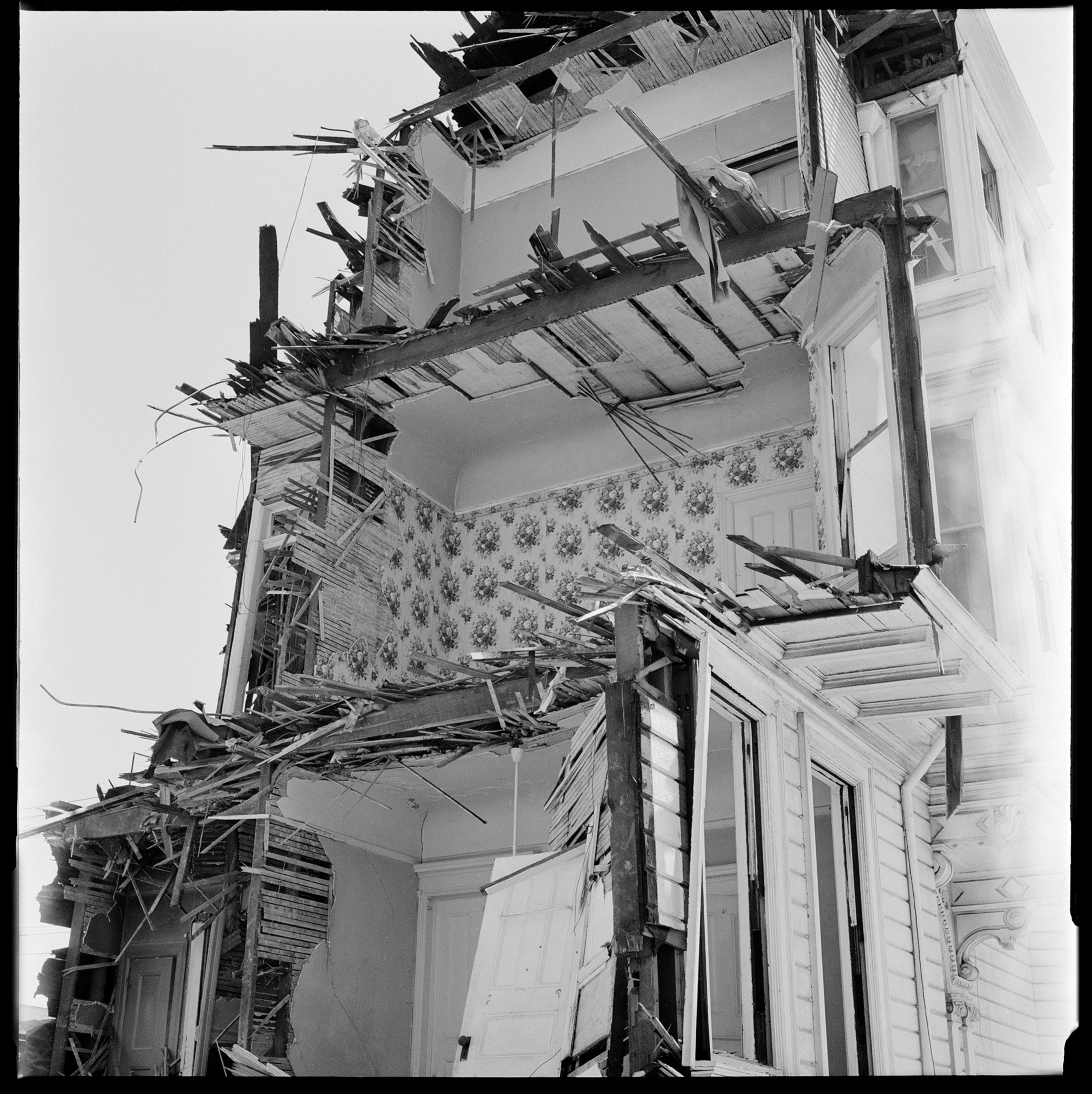 A damaged building with walls and floors partially collapsed, exposing wallpaper and structural beams.