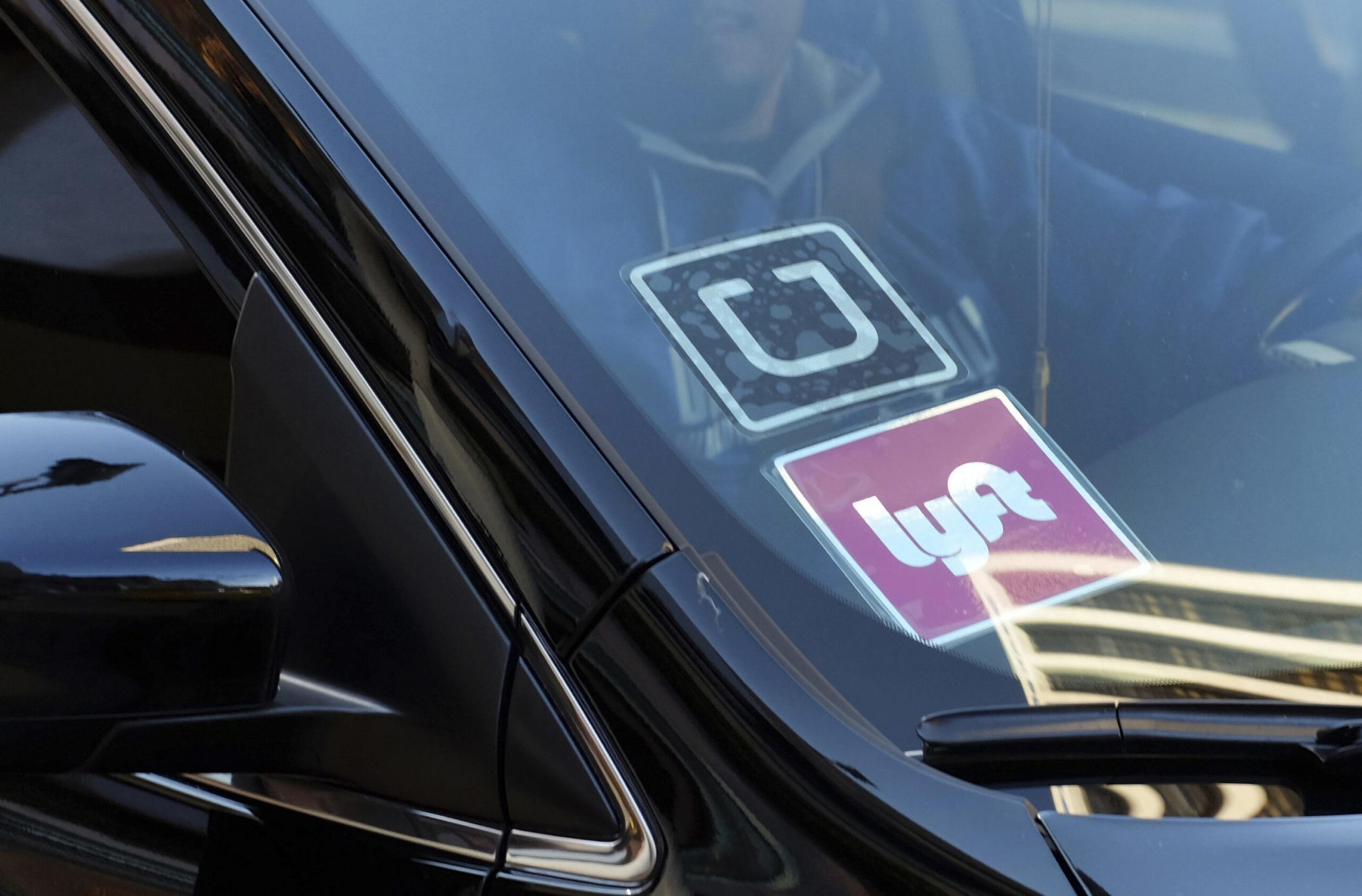 Uber and Lyft stickers are seen through a car windshield.