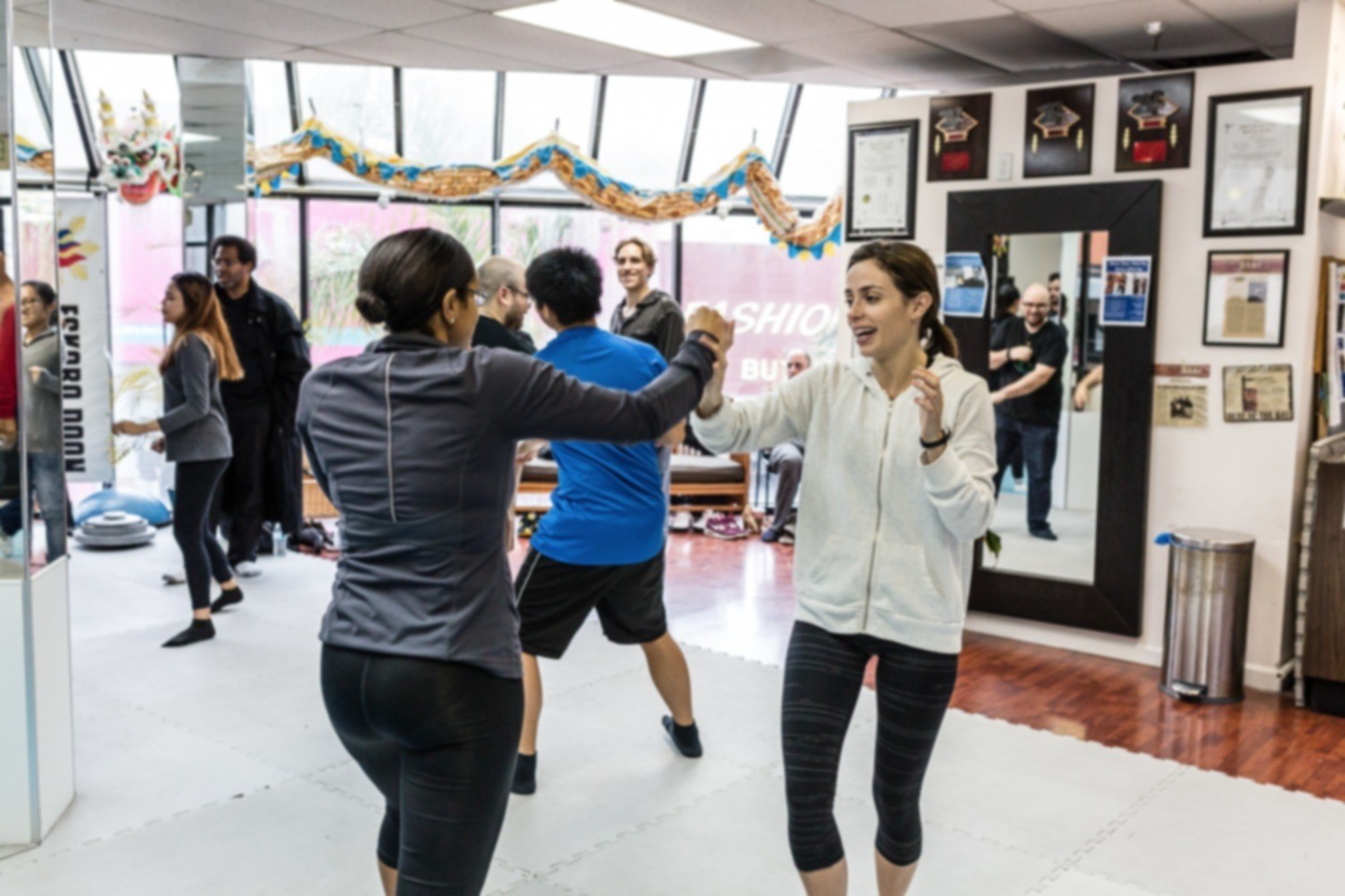 People in athletic wear practice martial arts moves together in a bright, decorated studio with certificates and awards on the wall.