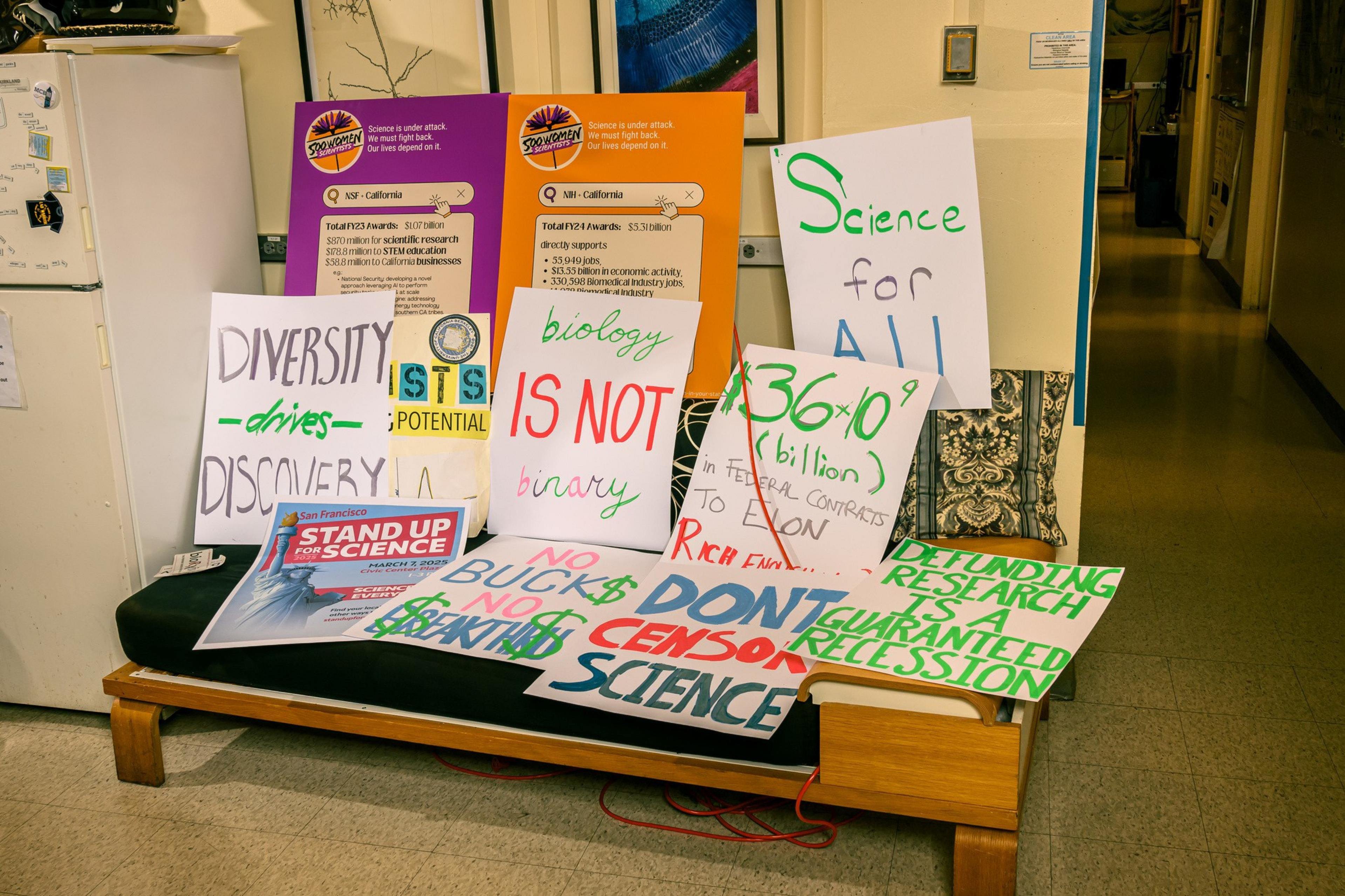 The image shows various protest signs advocating for science, diversity, and opposing censorship. Messages include &quot;Diversity drives discovery&quot; and &quot;Biology is not binary.&quot;
