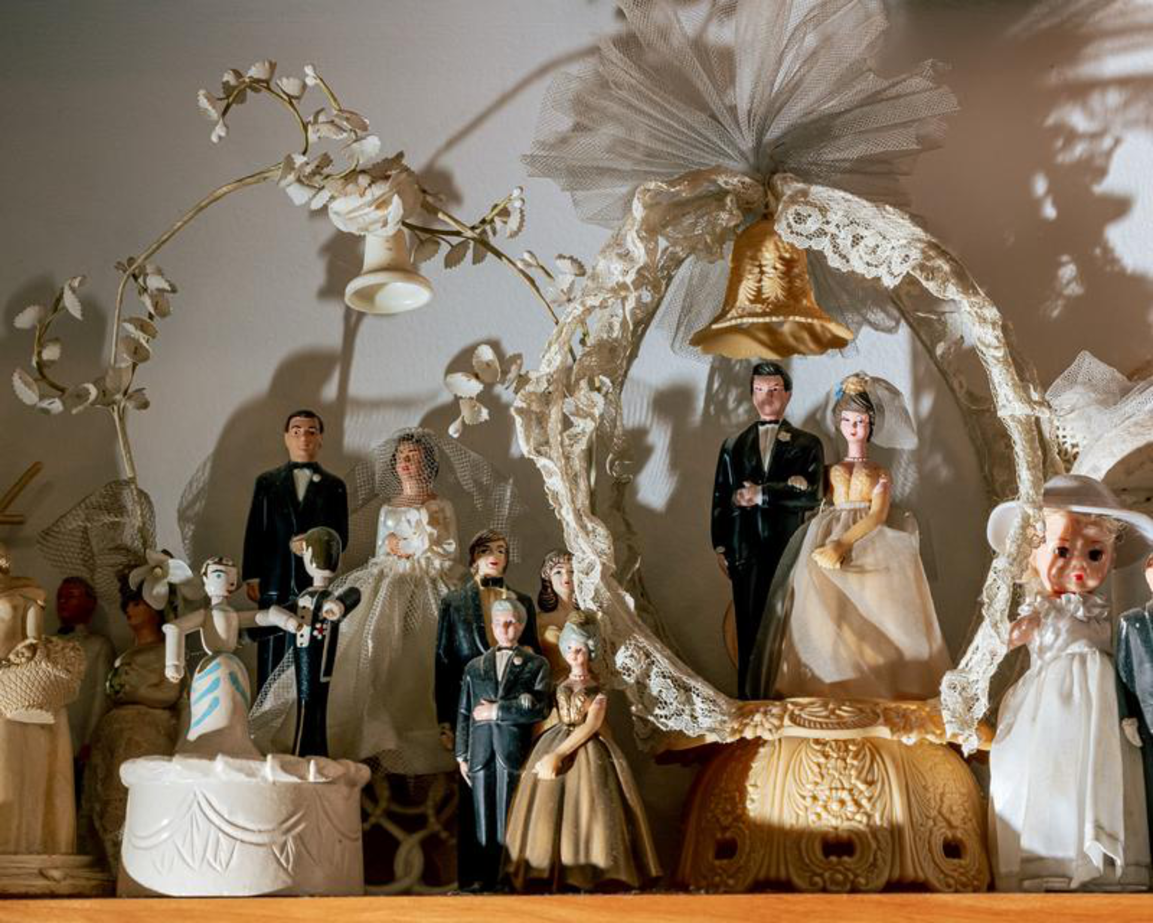 A collection of vintage wedding cake toppers includes several bride-and-groom couples in formal attire, some under lace arches with floral decorations.