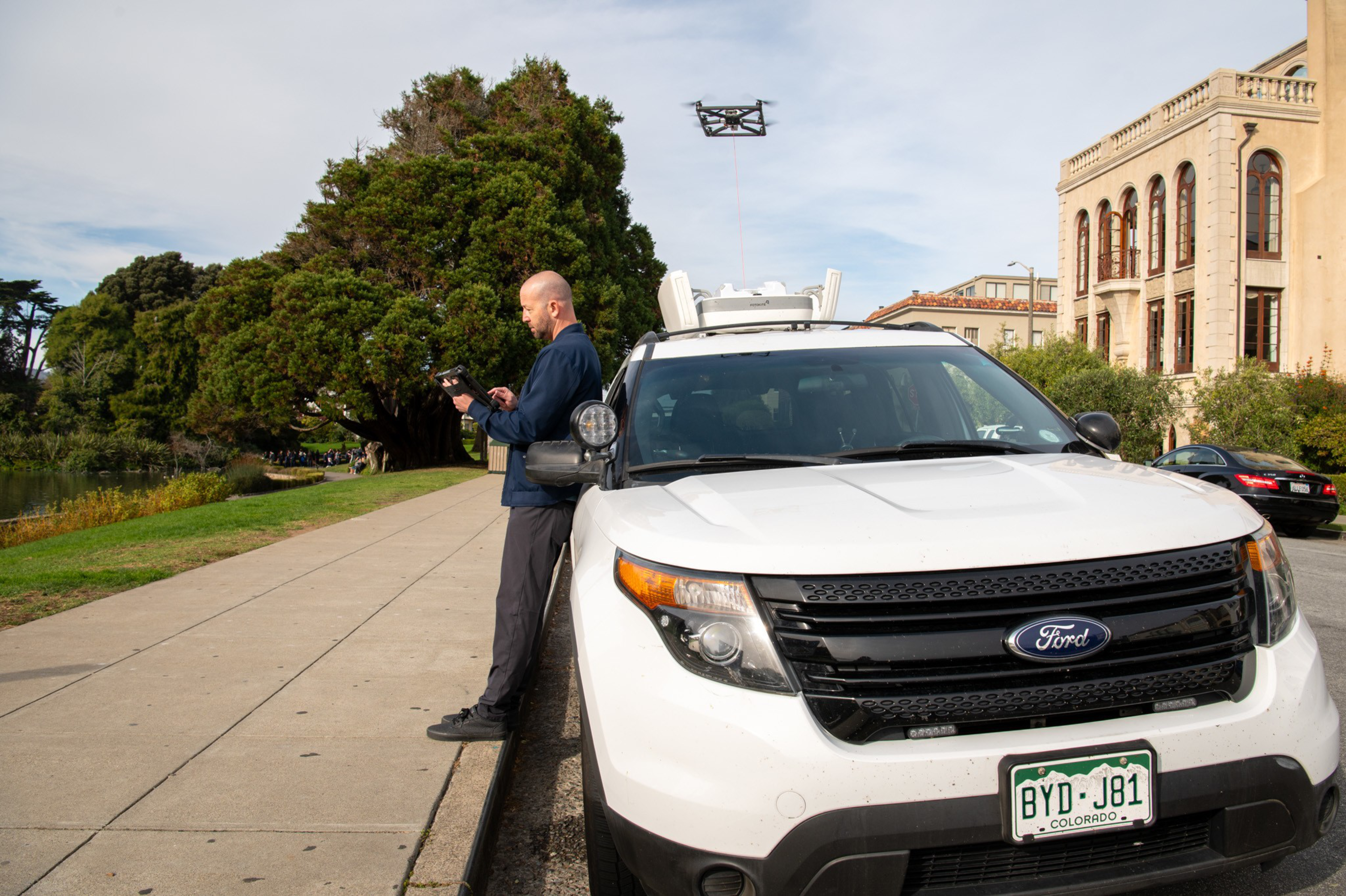 A man looks at an ipad with a drone in the background.