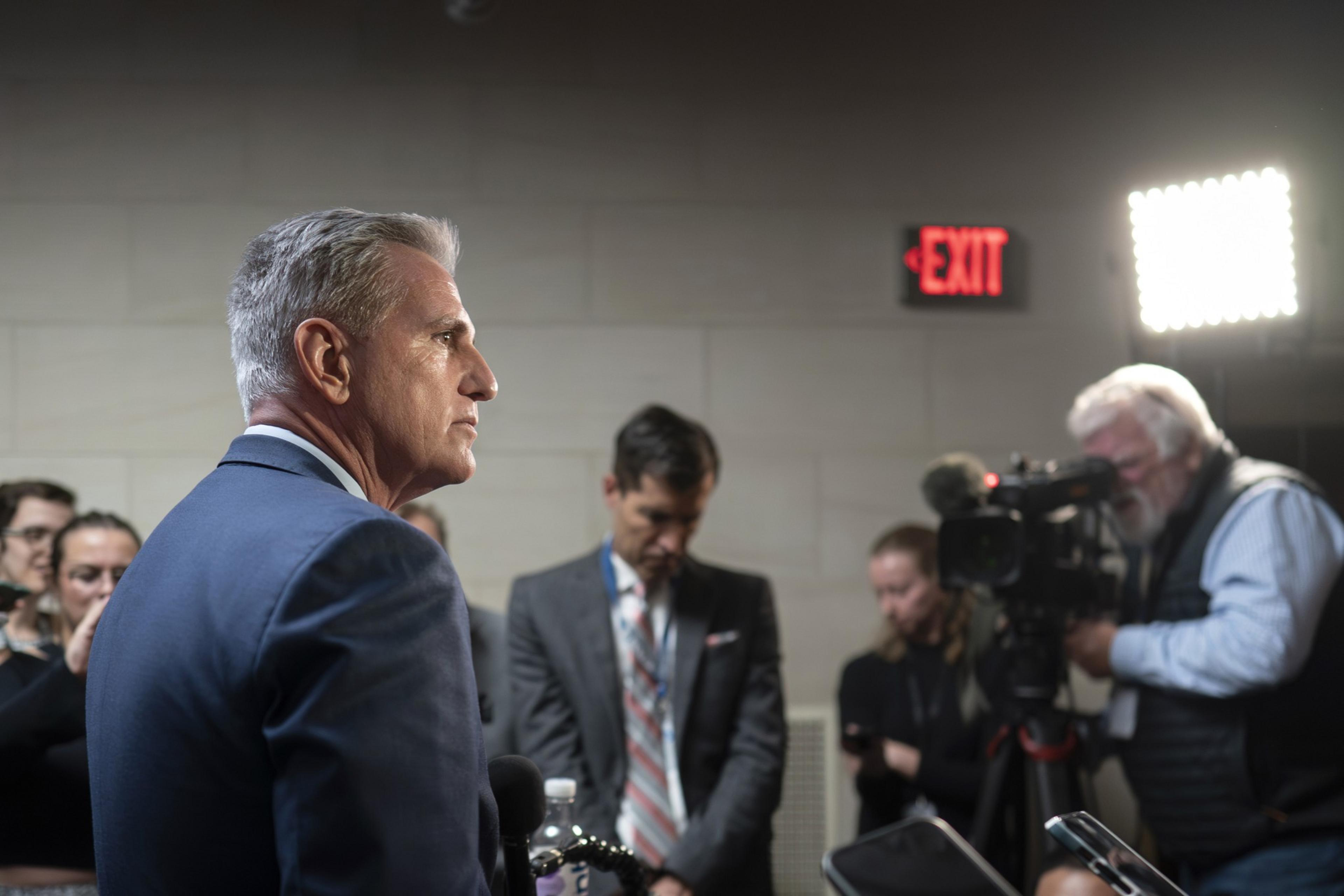 Kevin McCarthy stands before the press with an exit sign in the distance