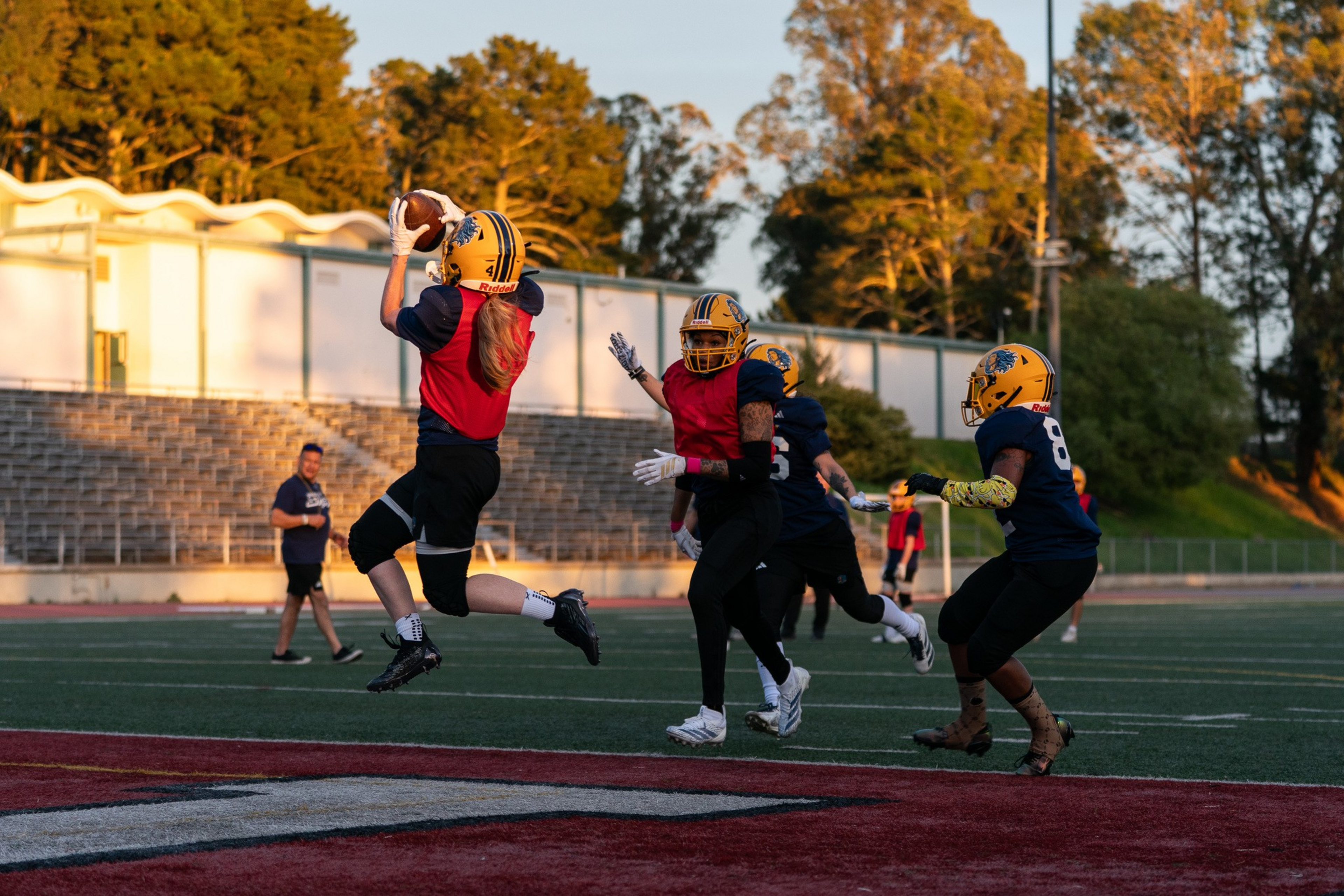 A football player in a red jersey and yellow helmet jumps to catch the ...