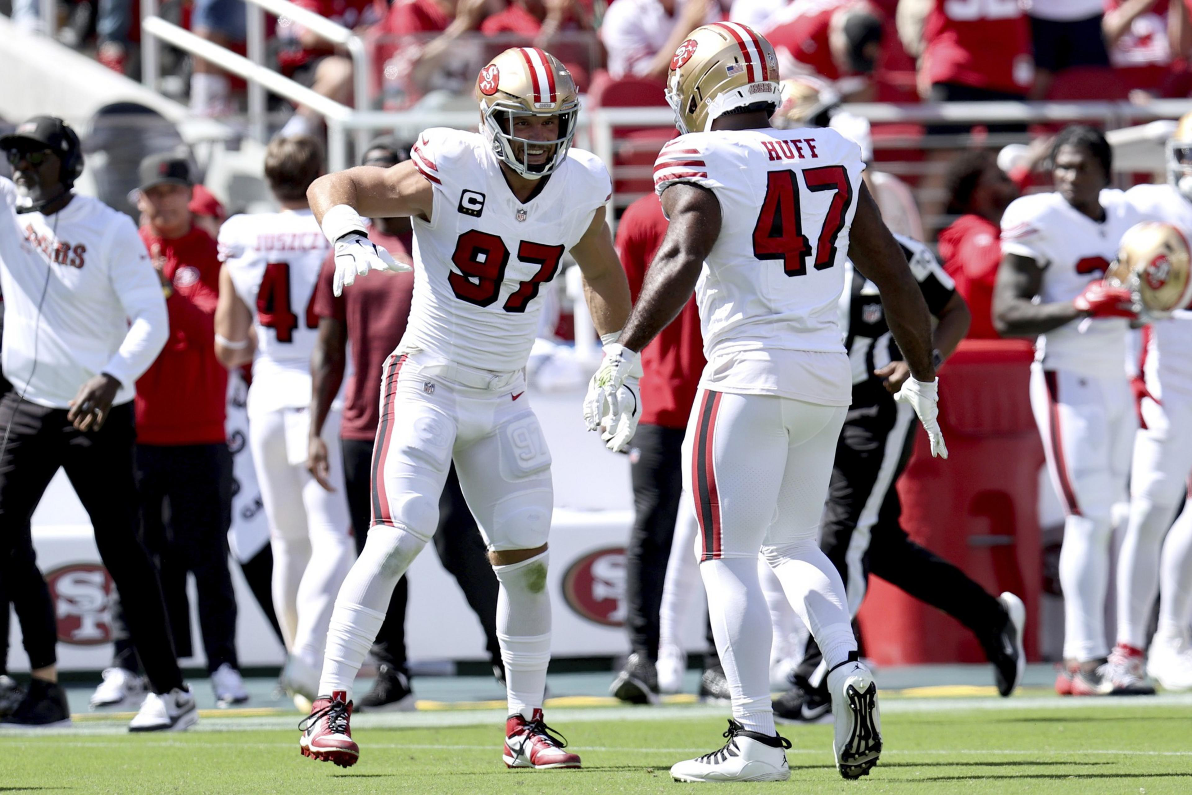 Two San Francisco 49ers players, wearing white uniforms with numbers 97 and 47, are celebrating on the football field during a game.
