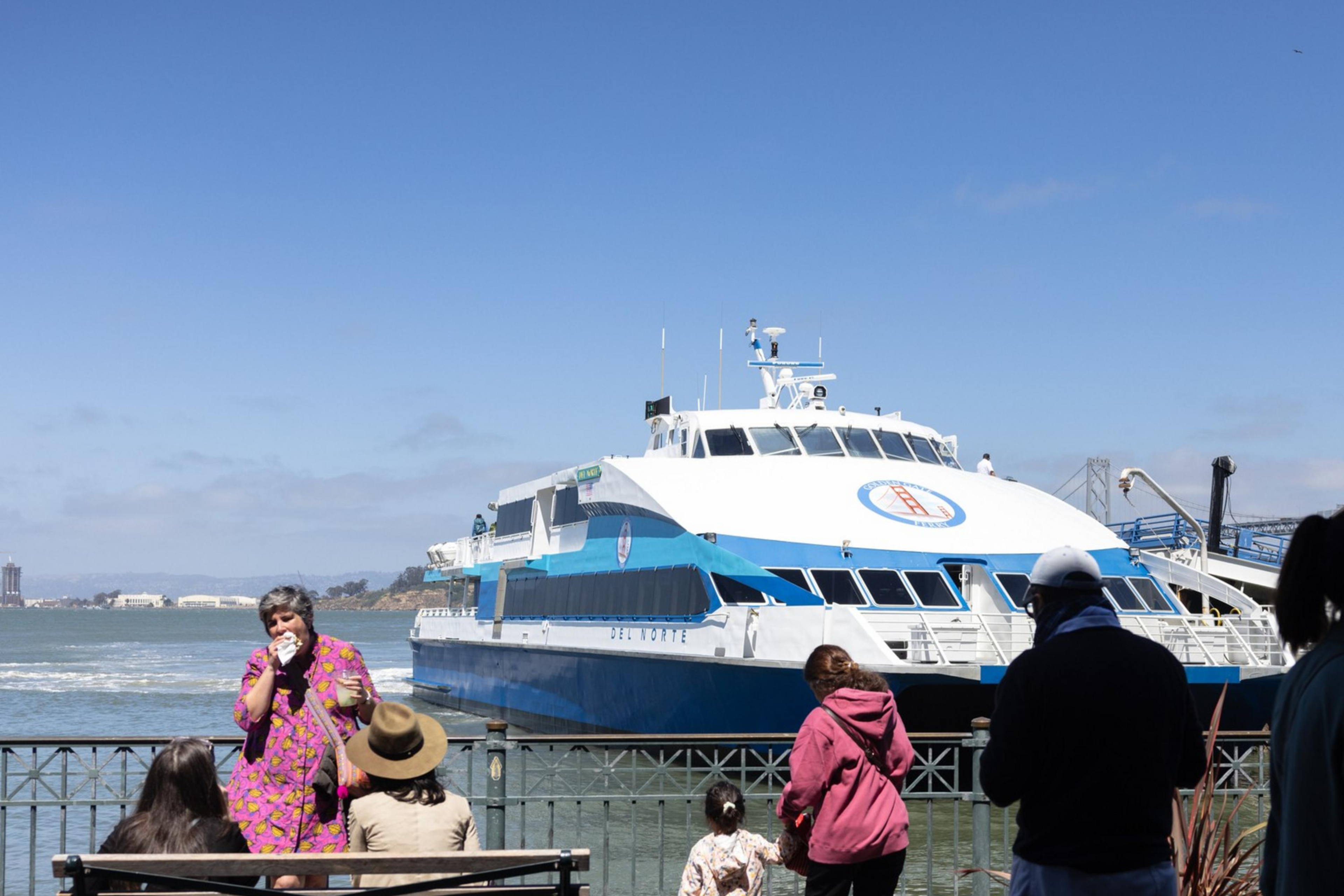 People on a dock observe a ferry boat on the water.