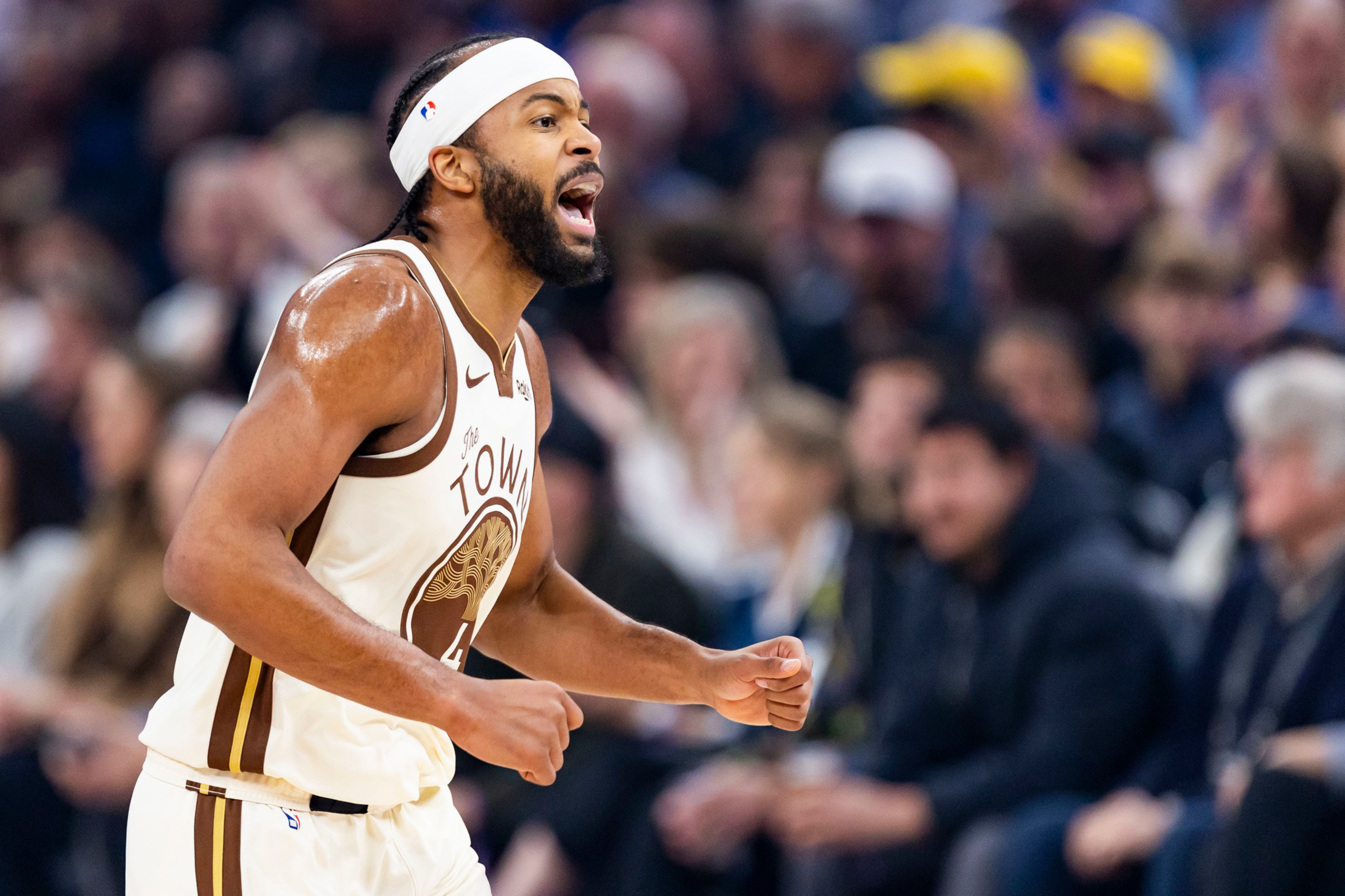A basketball player in a white and brown jersey with “The Town” shouts passionately, clenching his fists during a game.