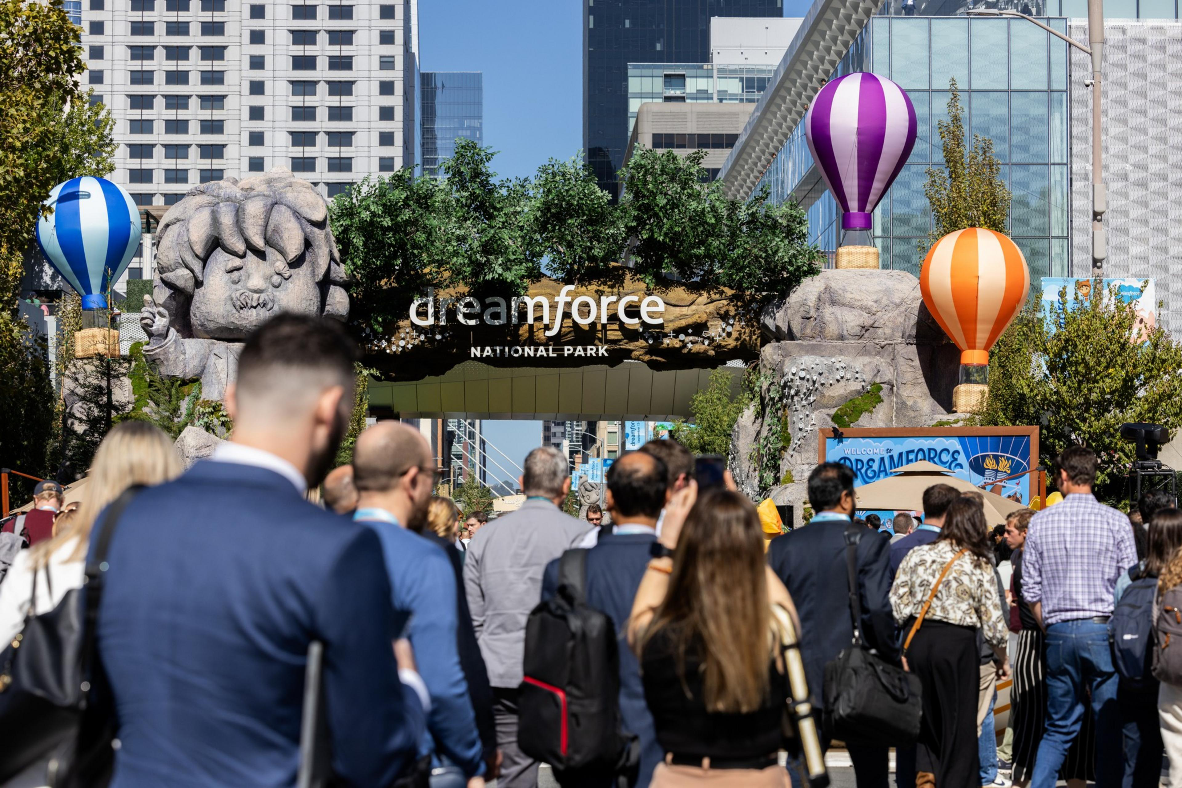 A crowd walks toward a large archway decorated with trees, a stone figure, and hot air balloons, with "dreamforce National Park" written on it.