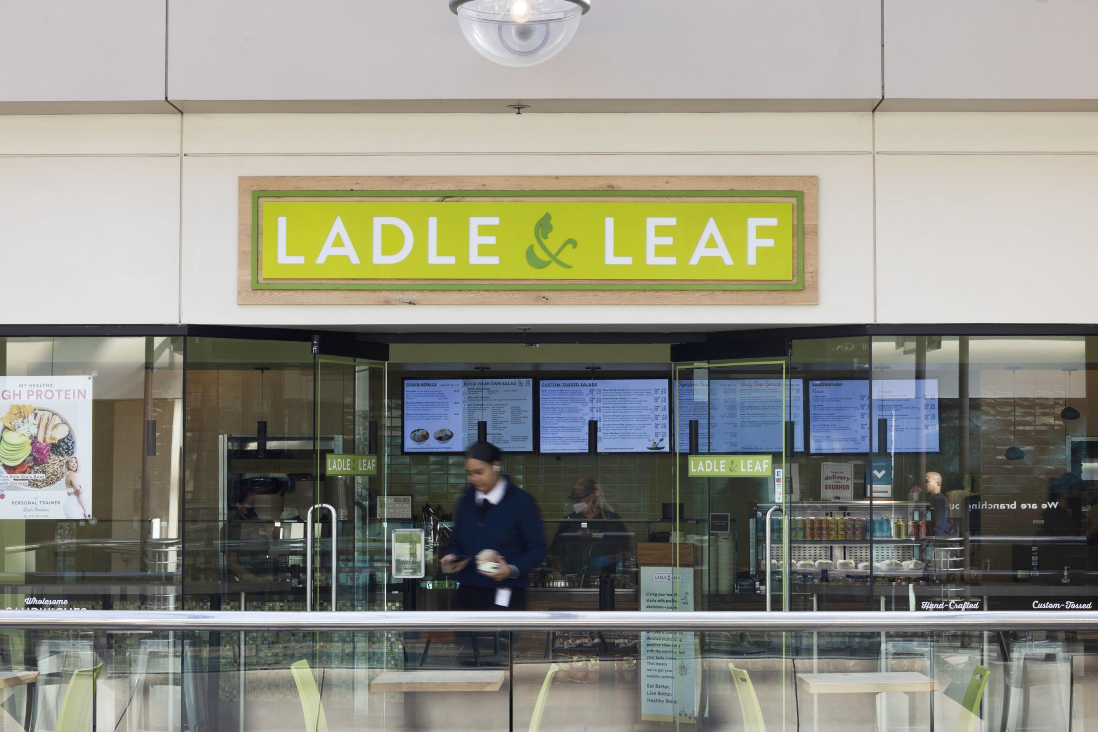 A restaurant named "Ladle & Leaf" with a bright green sign is located inside a mall, with glass doors and digital menu boards inside.