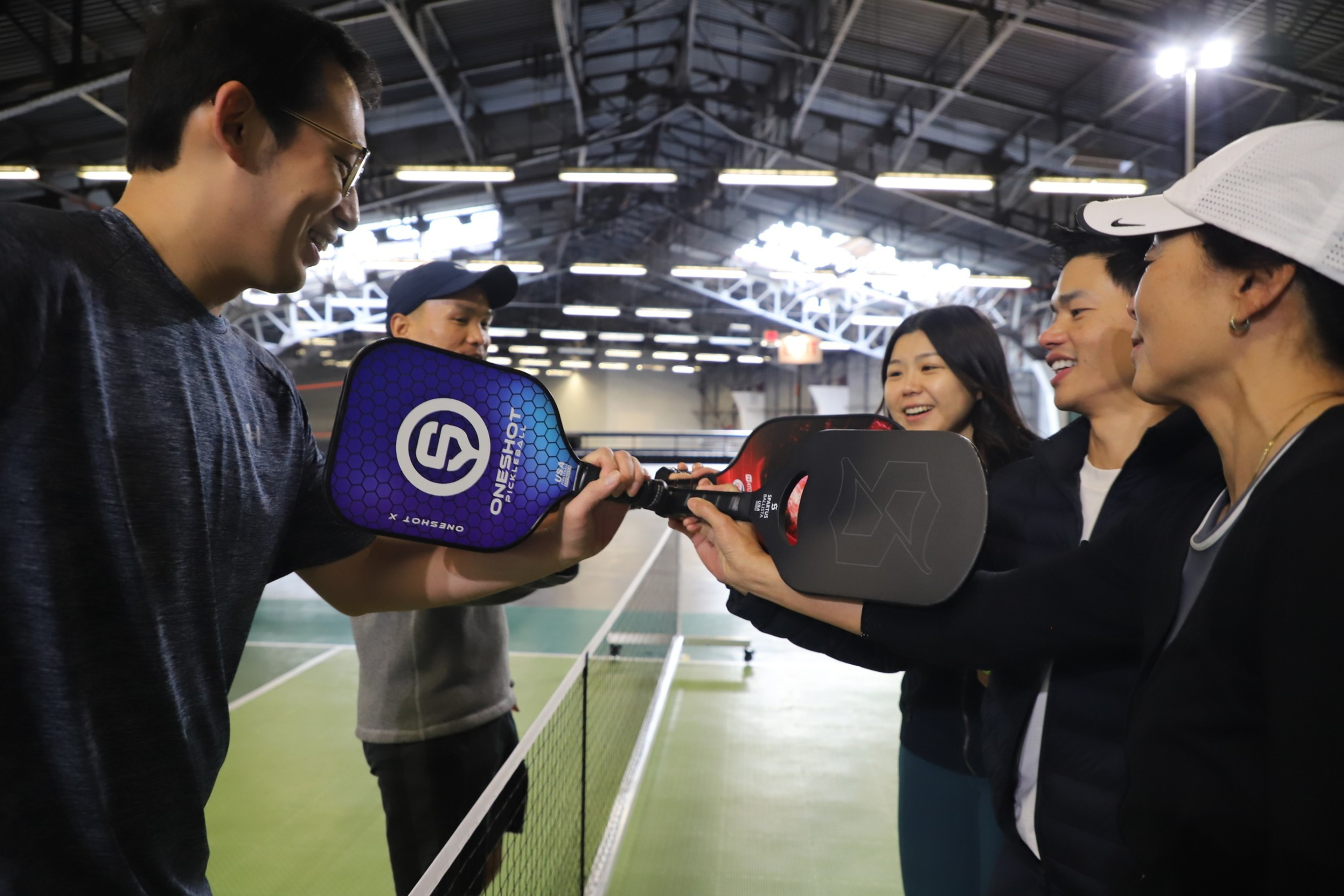 Four people with paddles are having fun on an indoor pickleball court.
