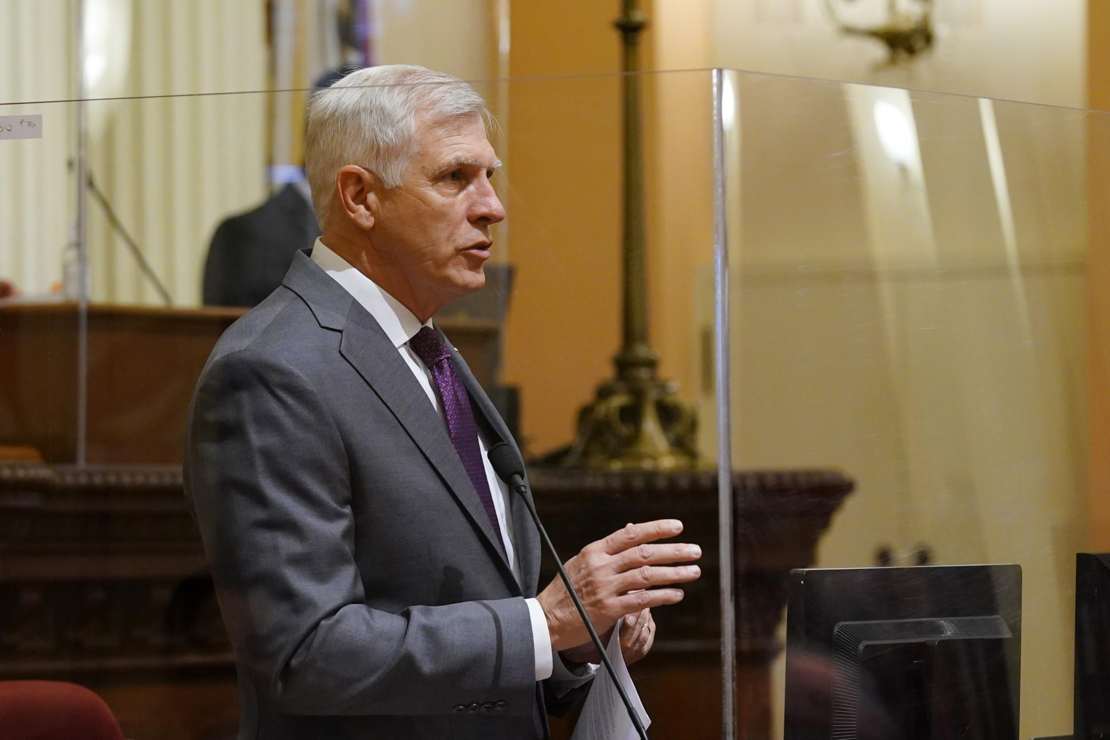 Man in gray jacket and tie speaks into microphone