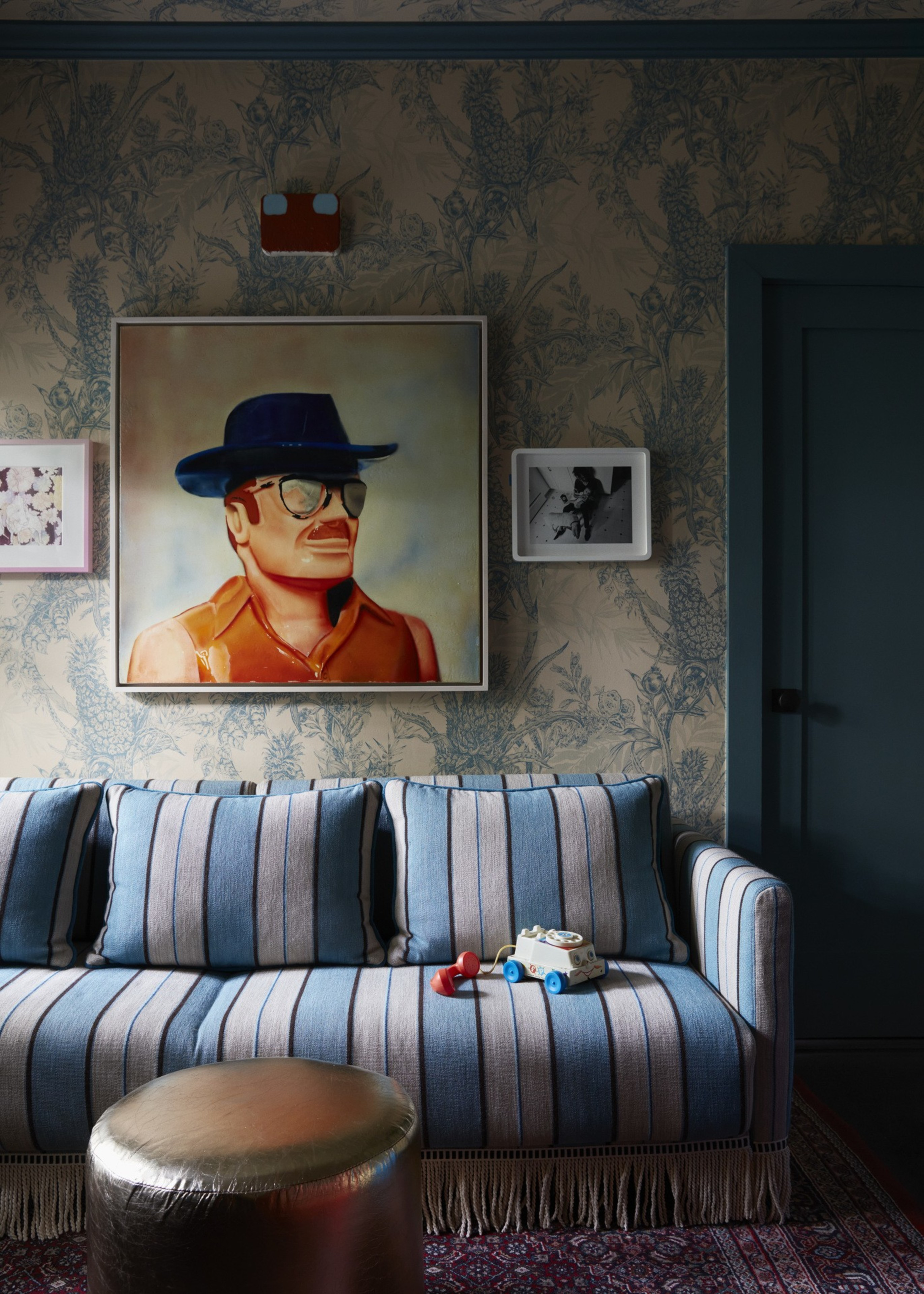 A striped blue and beige couch with toy cars sits under three framed pictures, including a colorful portrait of a man in a hat and sunglasses.