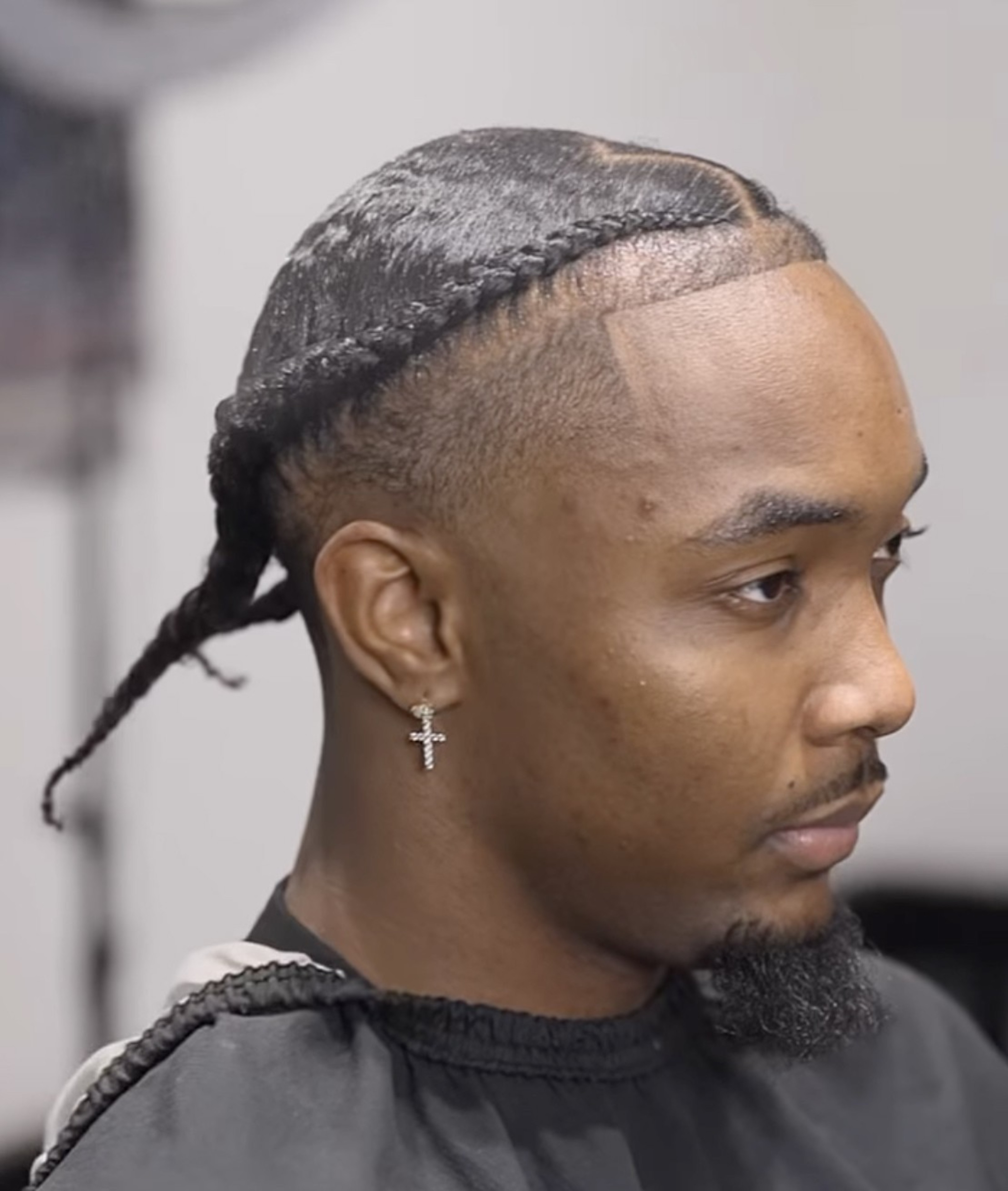 A man with braided hair, a shaped-up beard, and a cross earring.