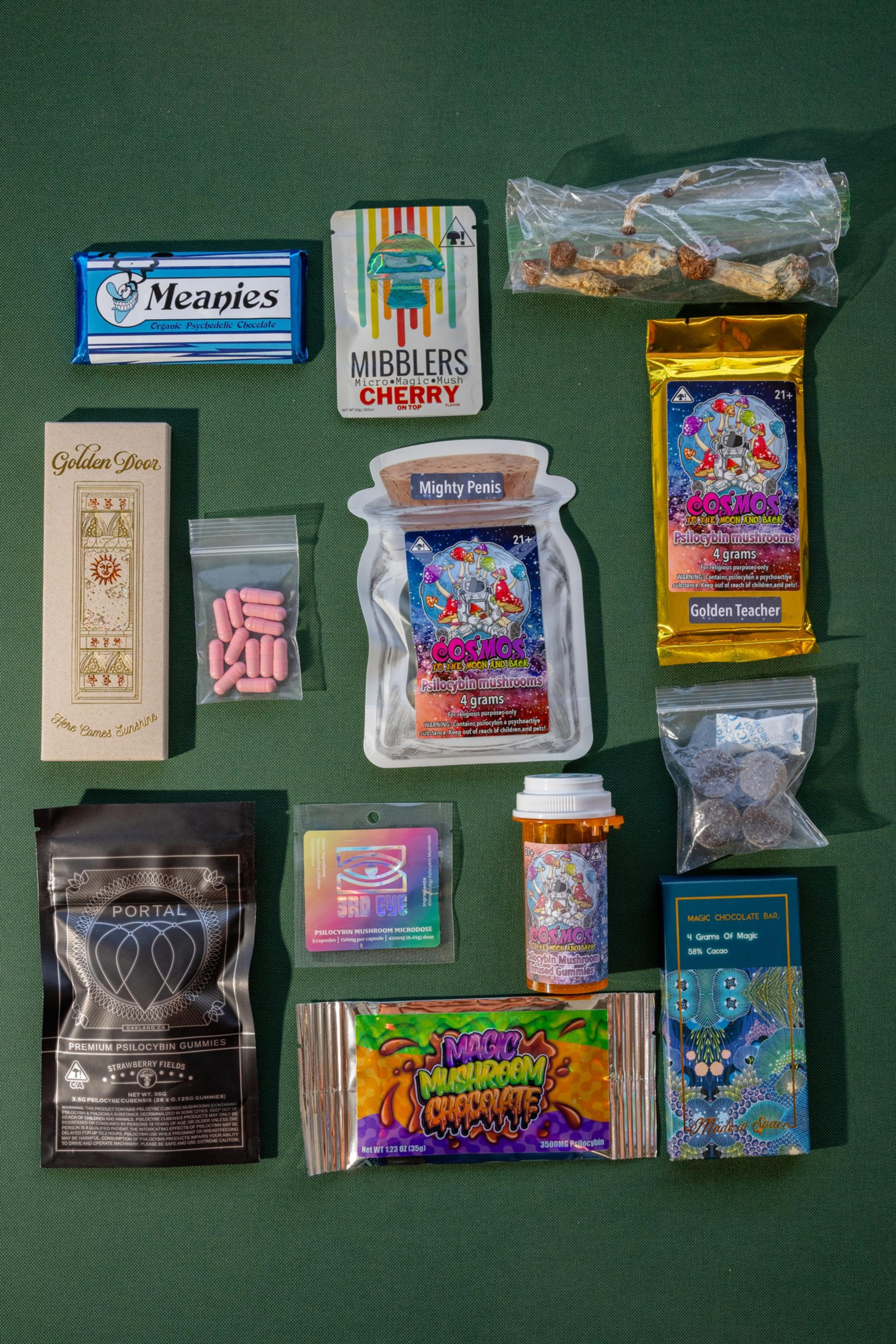 An assortment of colorful, psychedelic-themed packaged mushroom products are displayed on a green surface.