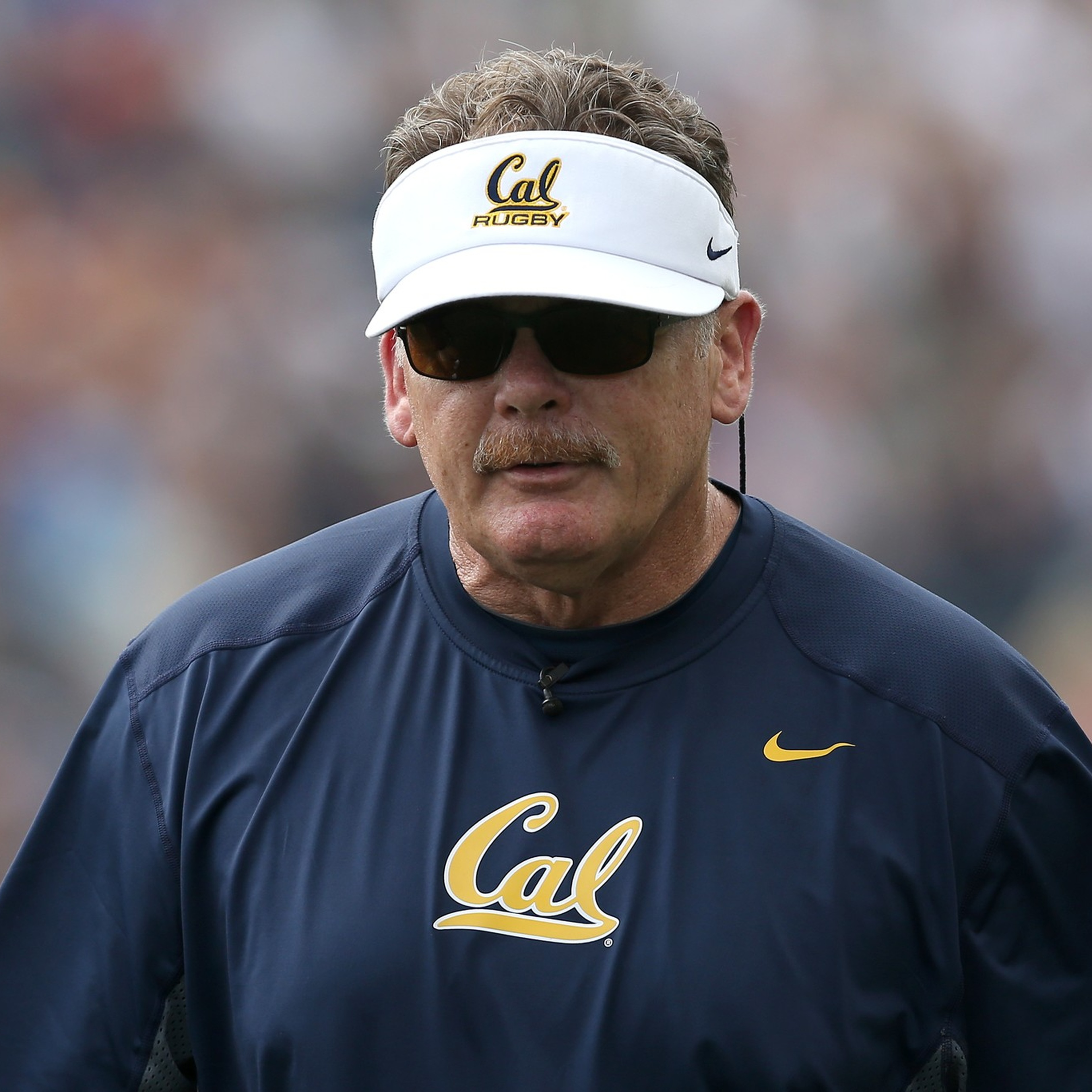 A man wearing sunglasses, a white visor reading 