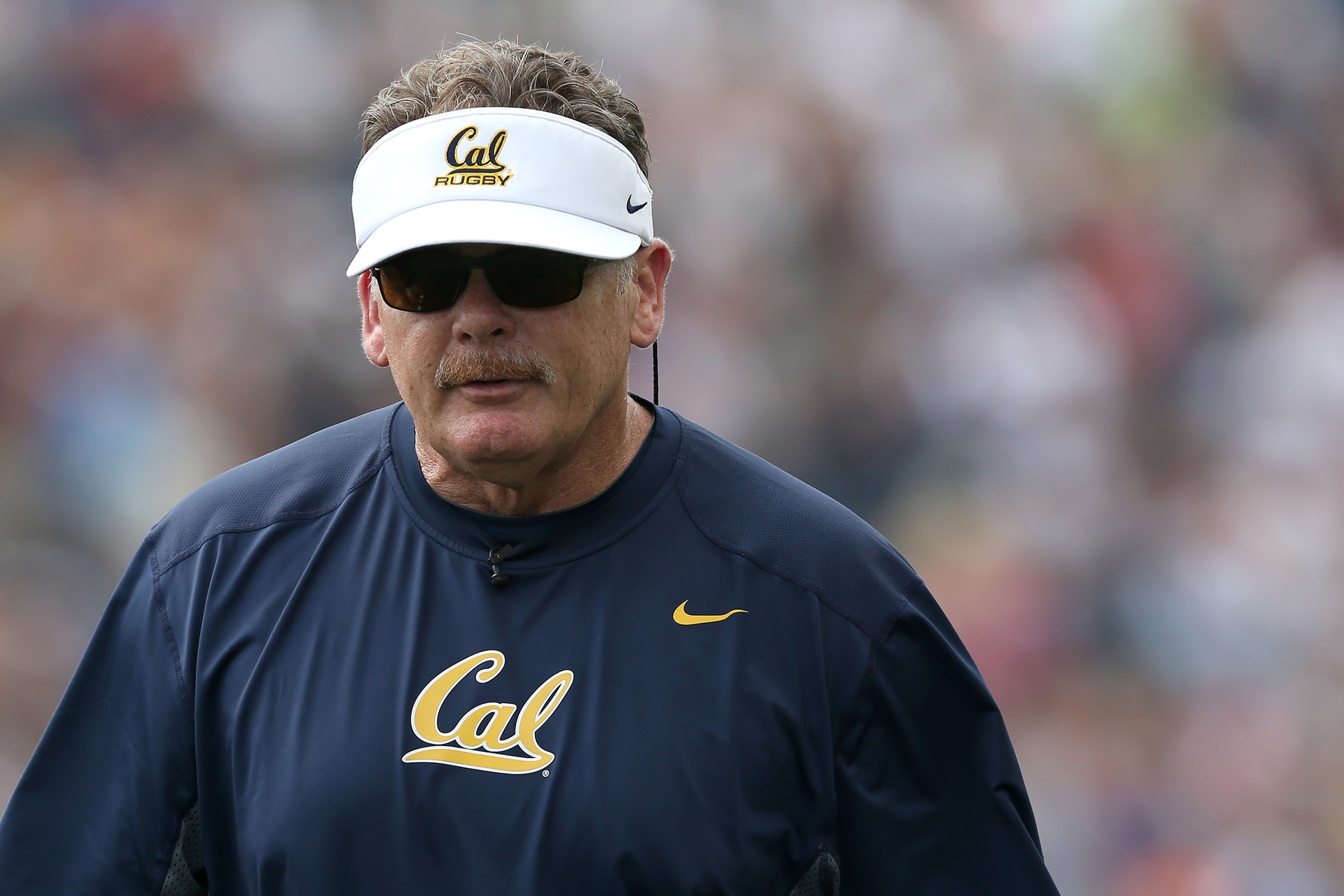 A man wearing sunglasses, a white visor reading 