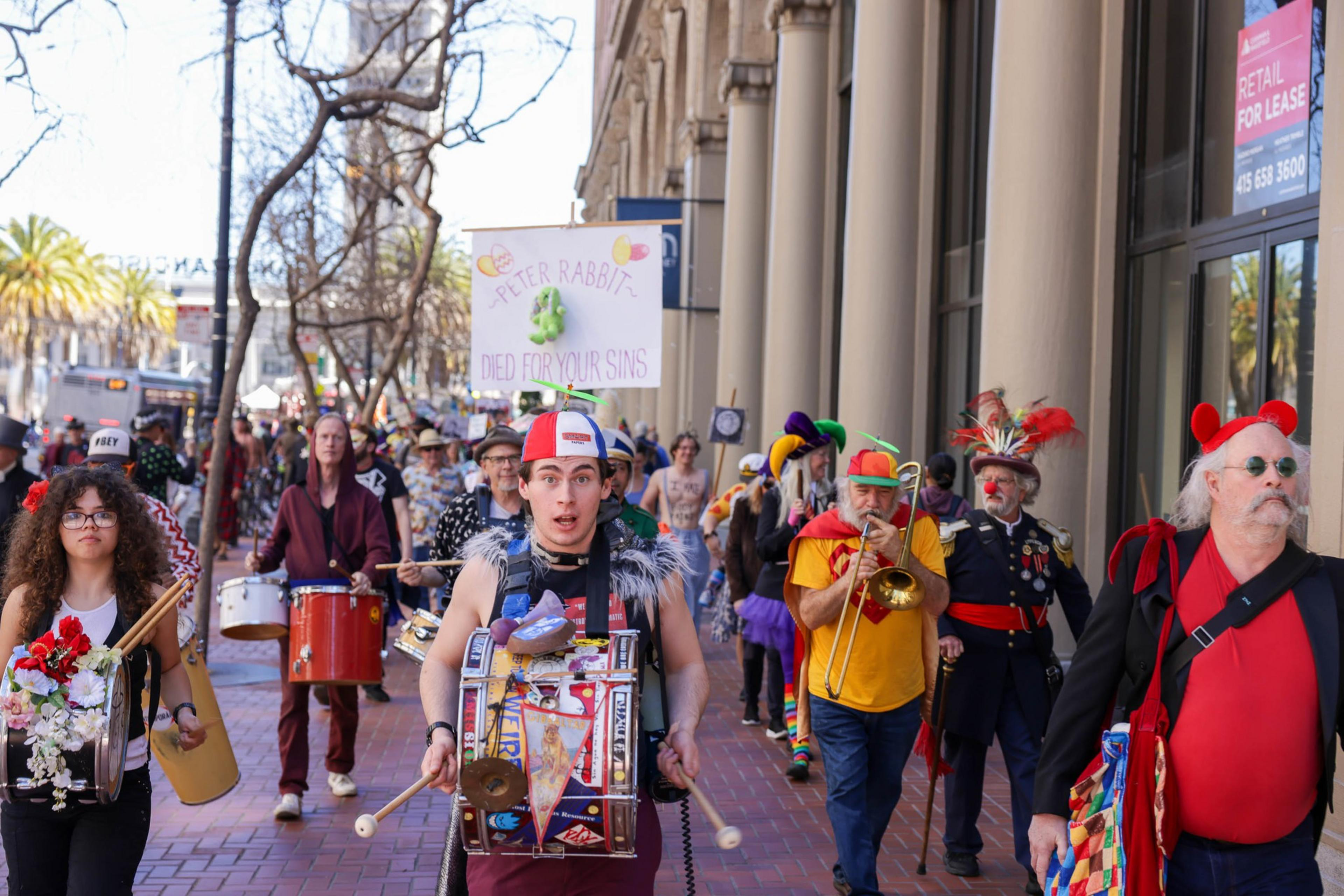 A colorful street parade with costumed participants, live music, and a humorous sign.