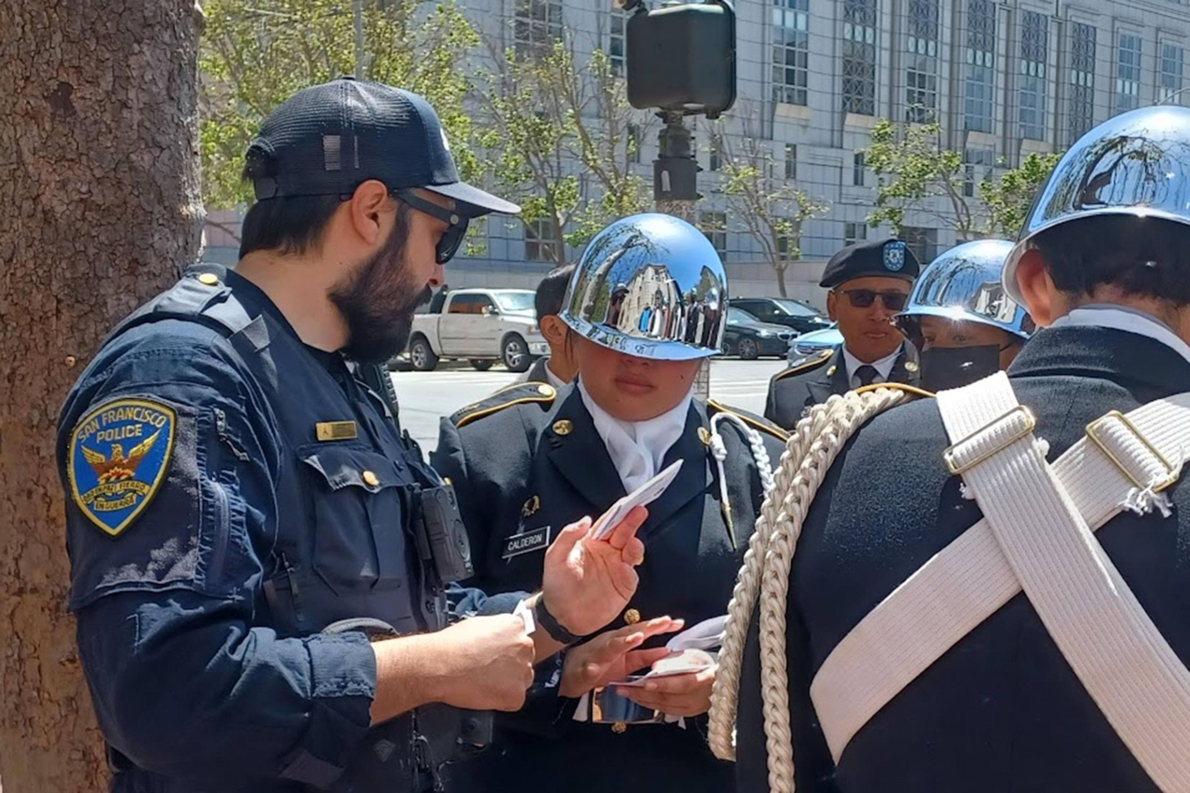 A San Francisco police officer checks IDs of uniformed individuals wearing shiny silver helmets and black jackets with white straps.