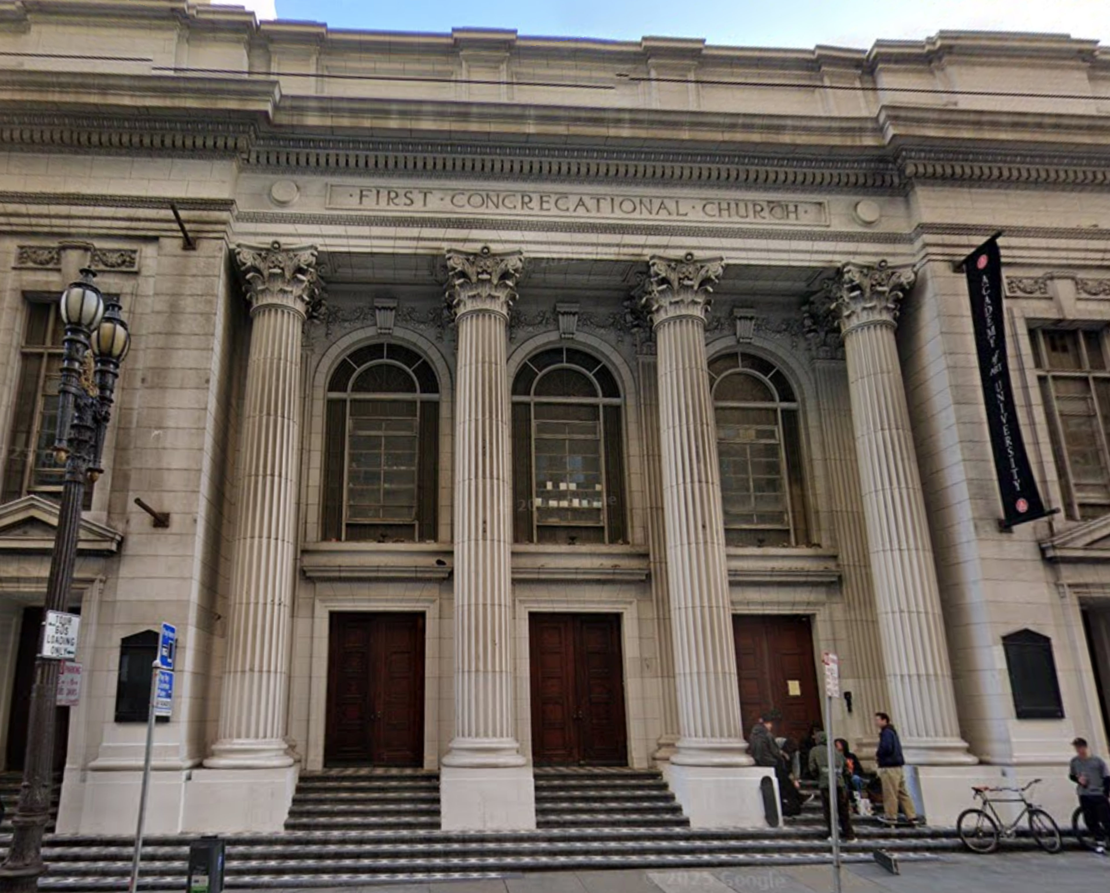 A grand neoclassical building with four tall Corinthian columns in front, three large wooden doors, and a sign reading “First Congregational Church.”