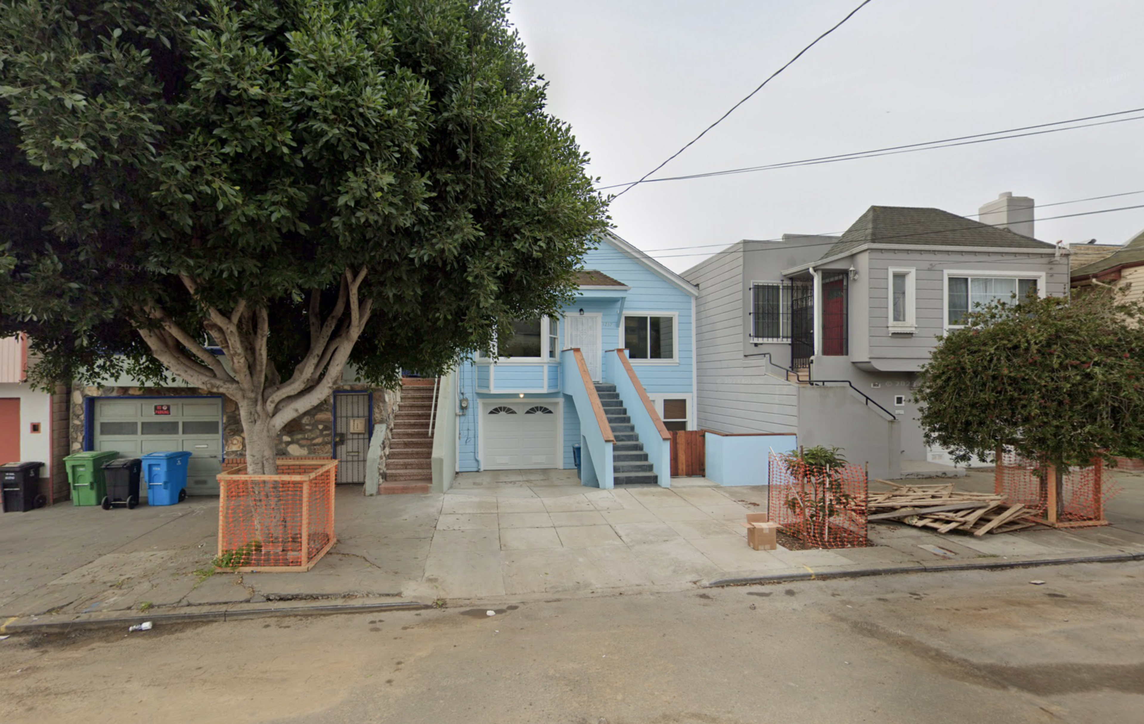 A house faces the street and construction debris lies on the sidewalk.