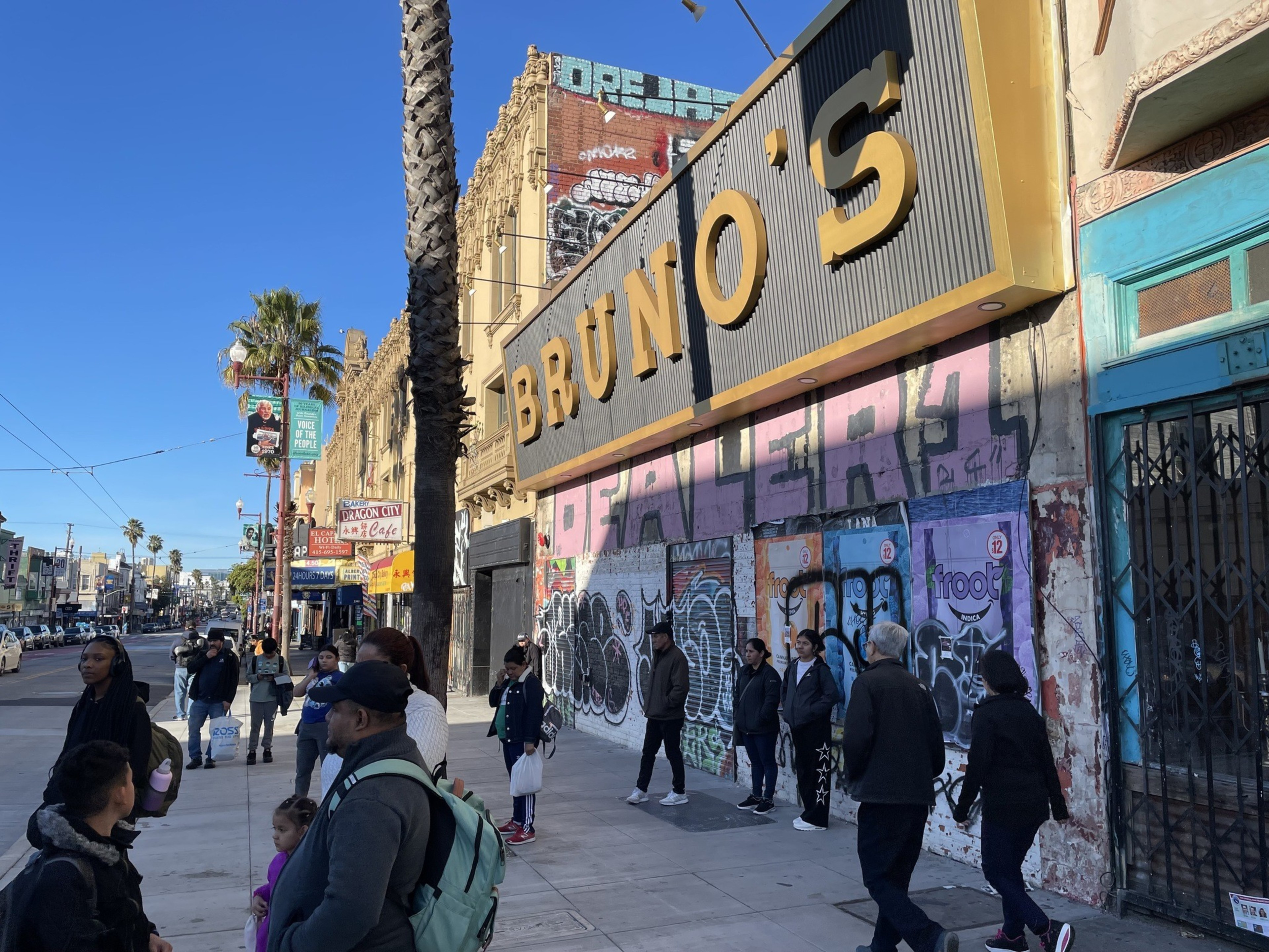 People walk past a boarded-up nightclub covered in graffiti.