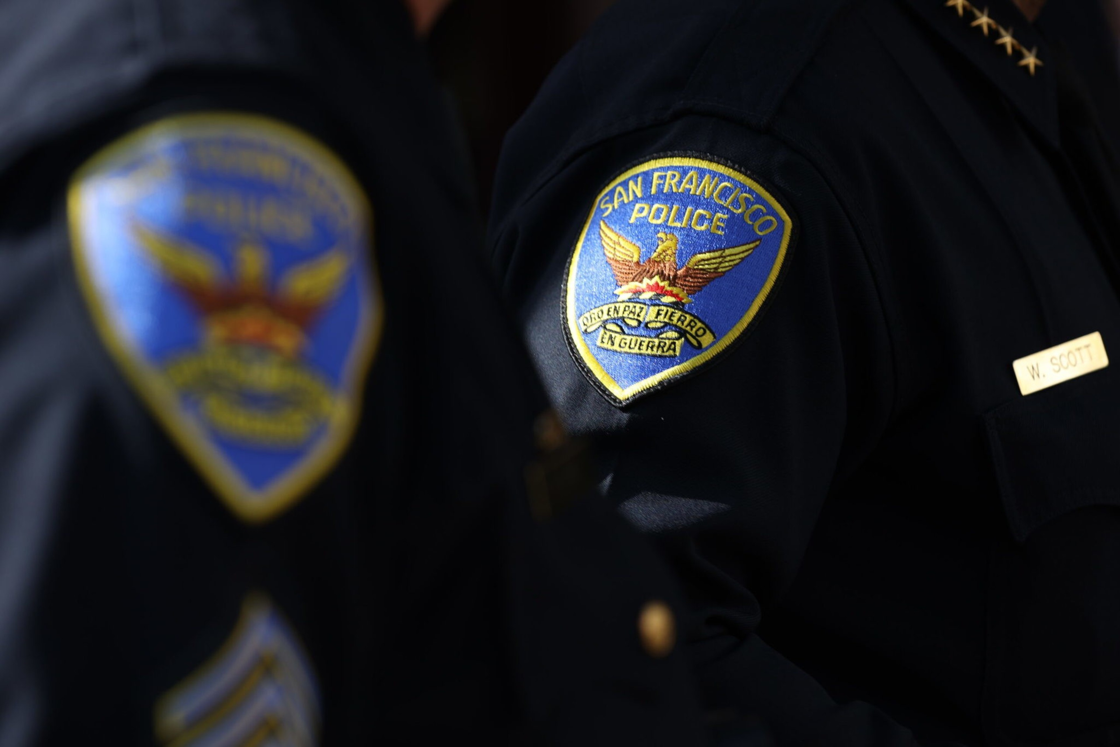 Two police officers in dark uniforms display San Francisco Police Department patches on their sleeves, with one officer's name tag reading "W. Scott."