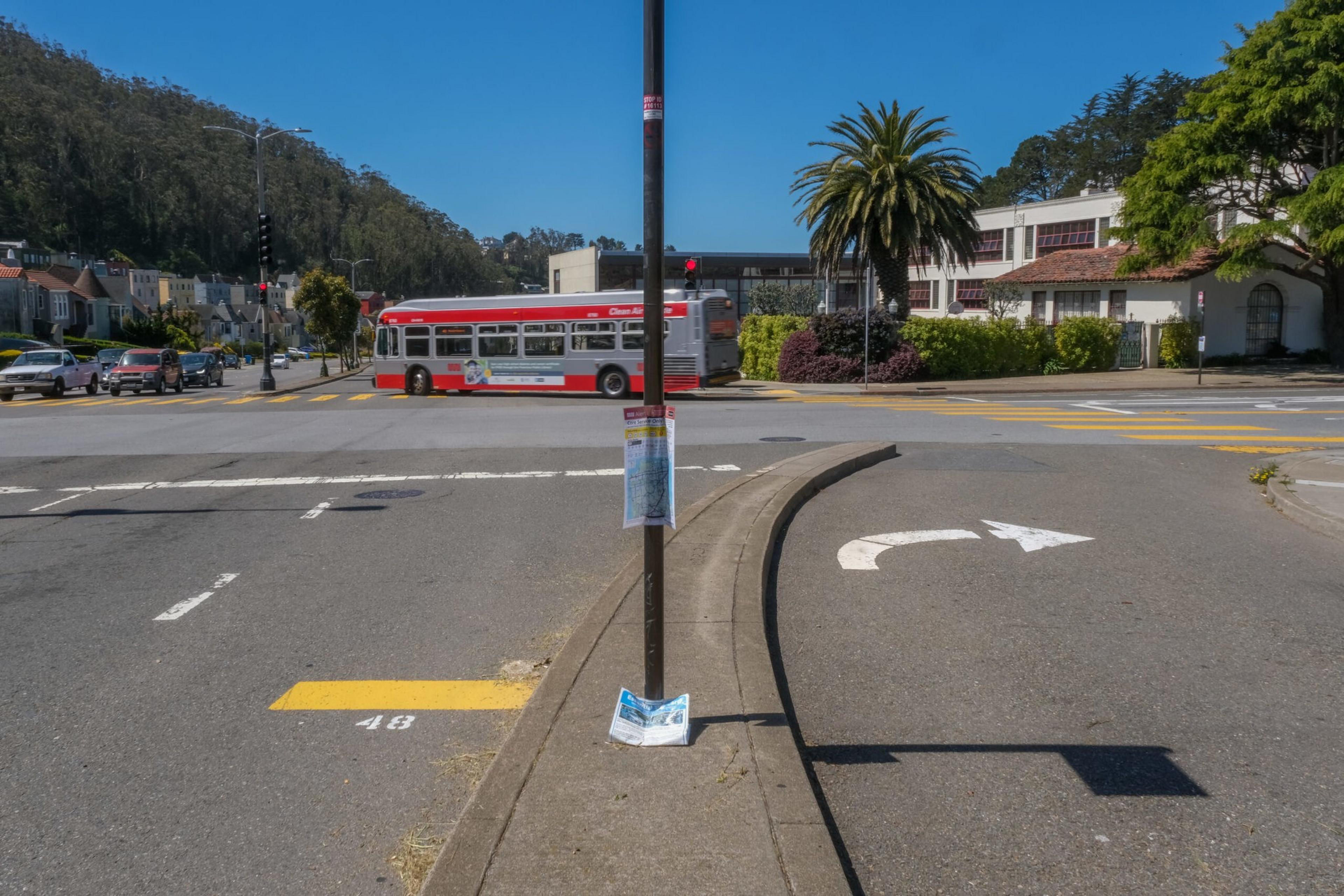 A red and white bus crosses an intersection on a clear day, with a palm tree and buildings in the background and a right-turn arrow painted on the road.