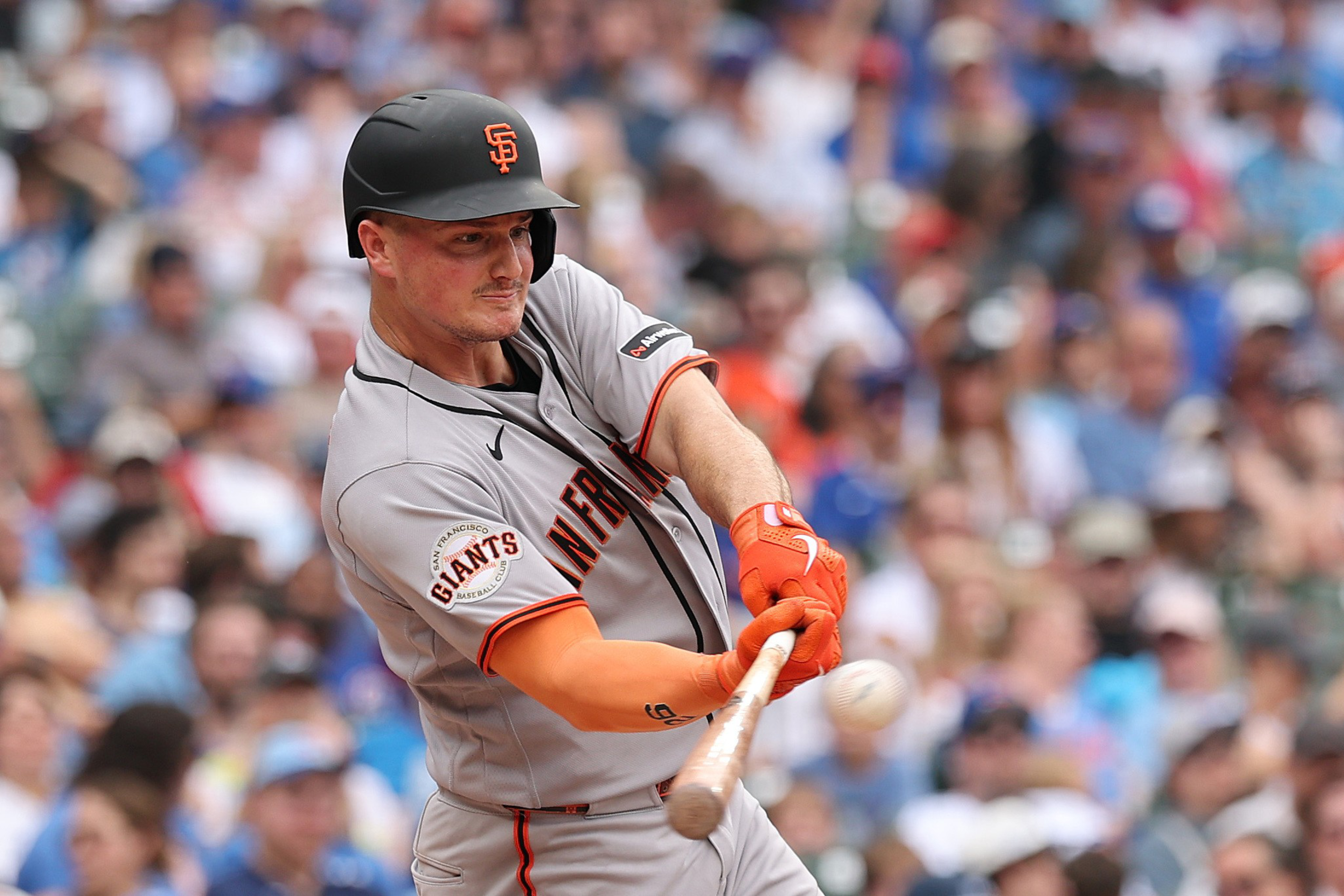 A San Francisco Giants baseball player wearing gray and orange swings a bat, making contact with a ball during a game.