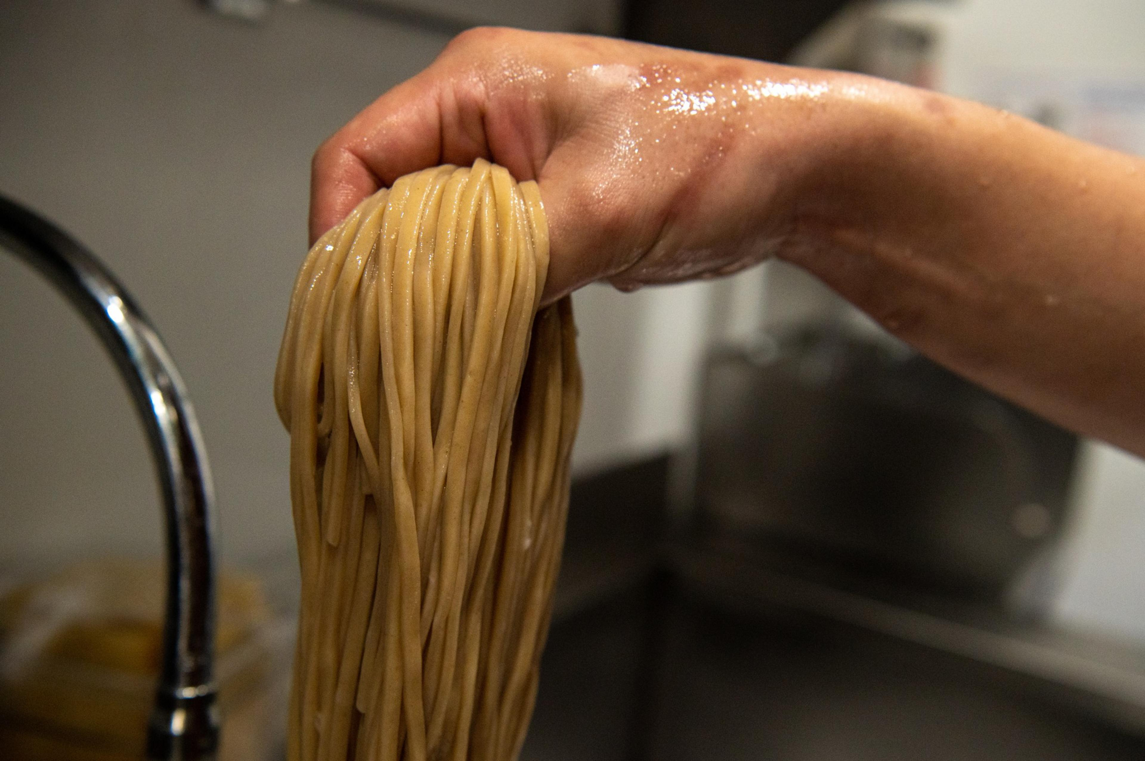 A hand holds wet noodles.