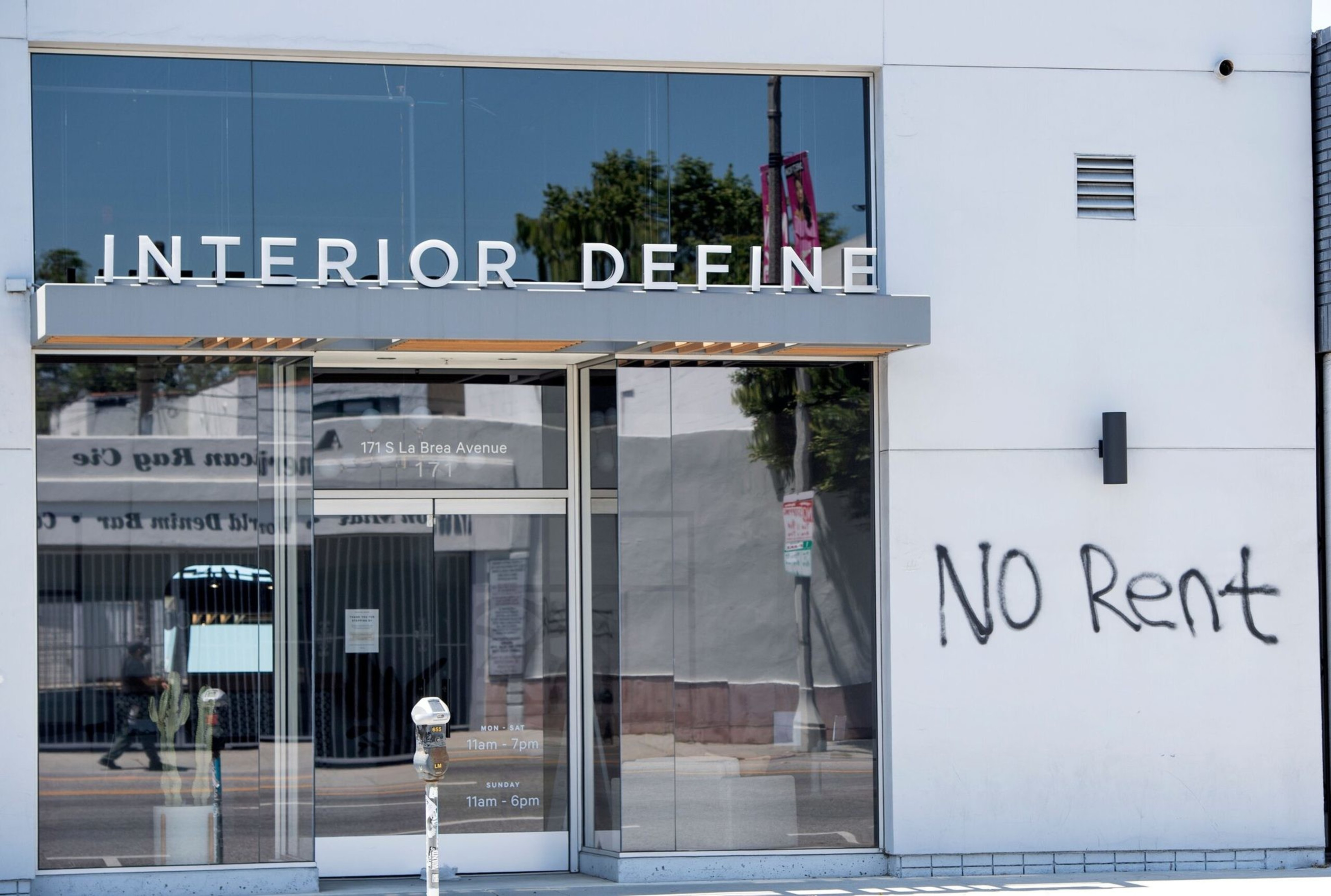 A store named Interior Define has large glass windows, and the words "NO Rent" are spray-painted in black on the white wall beside the entrance.