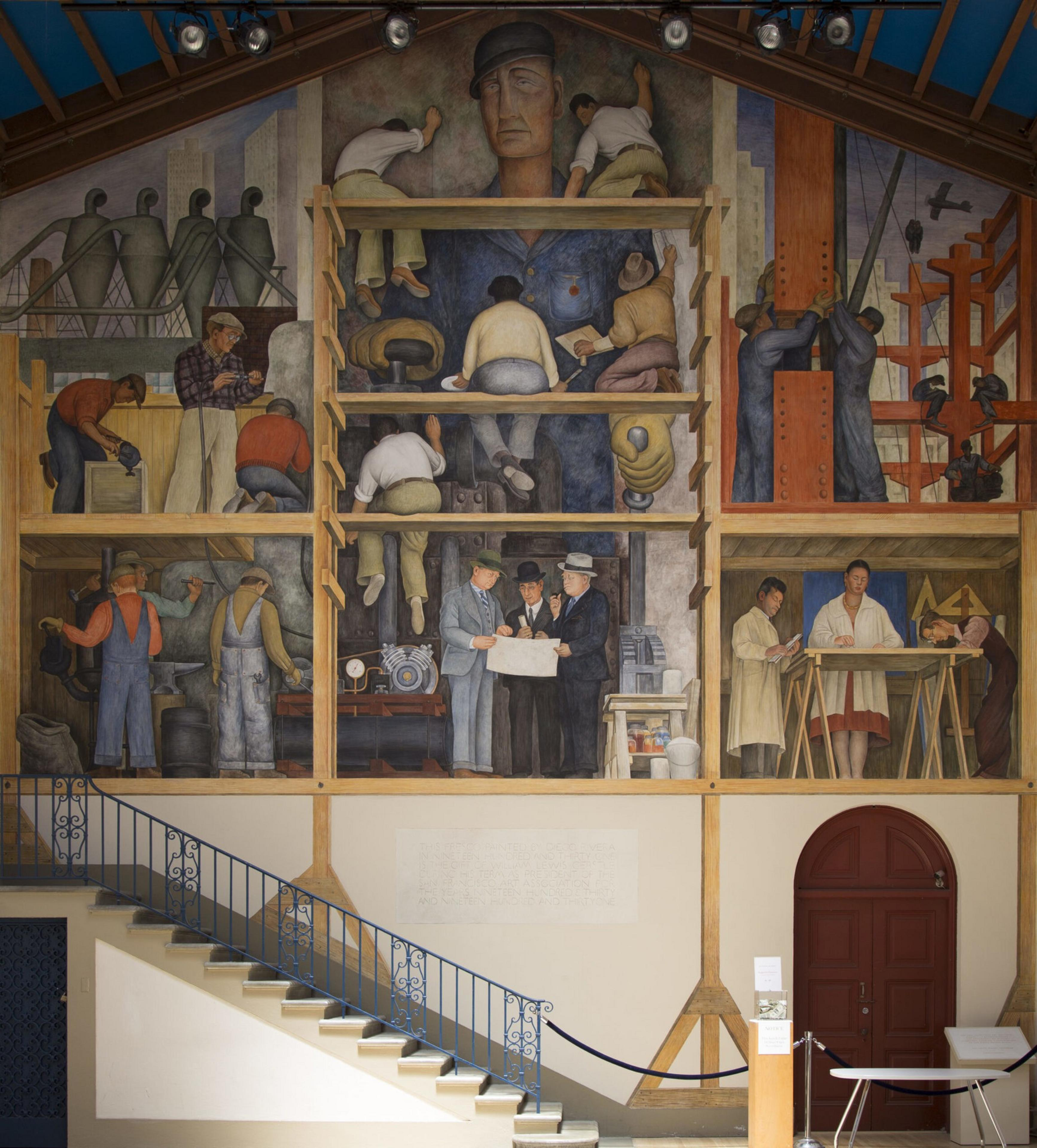 A mural depicts workers and engineers collaborating on construction and industry, with figures painting, assembling machinery, and planning blueprints across multiple levels.