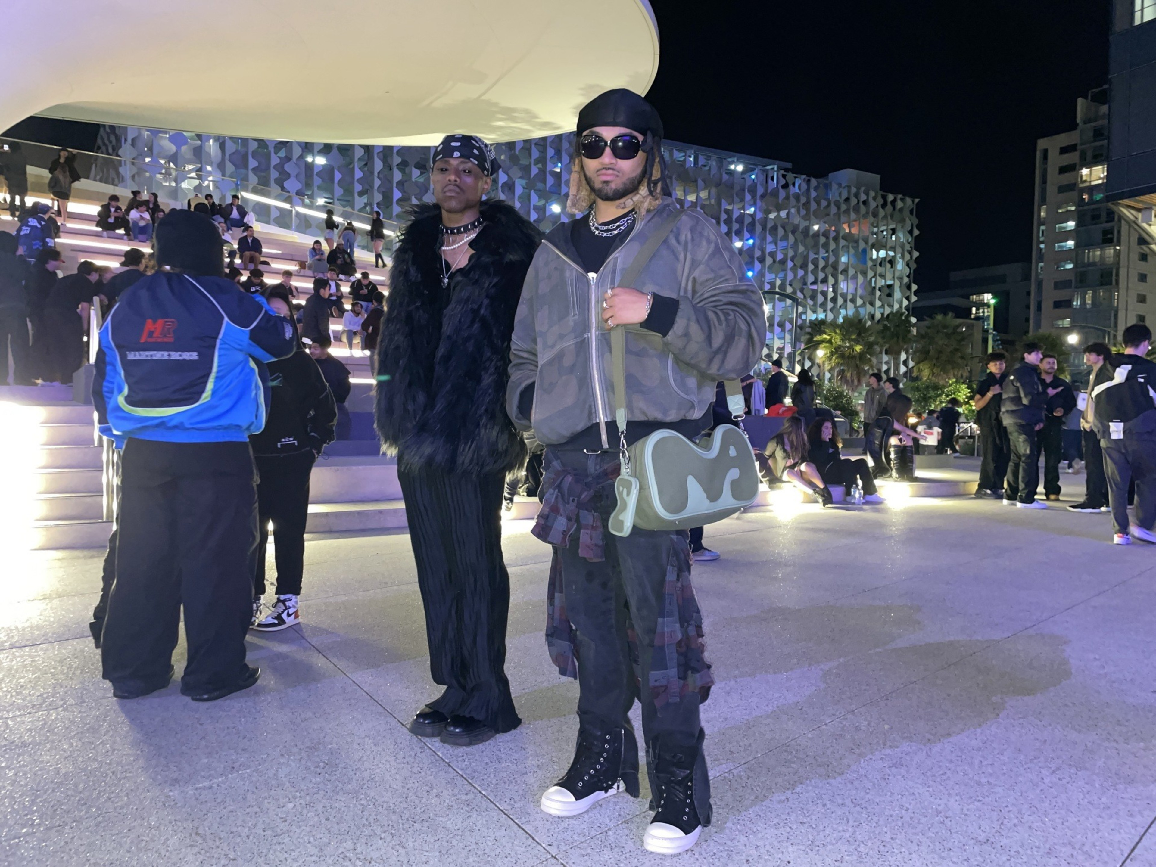 Two stylish individuals posing at a night event, one in a fur coat, the other in a denim jacket and camo pants.