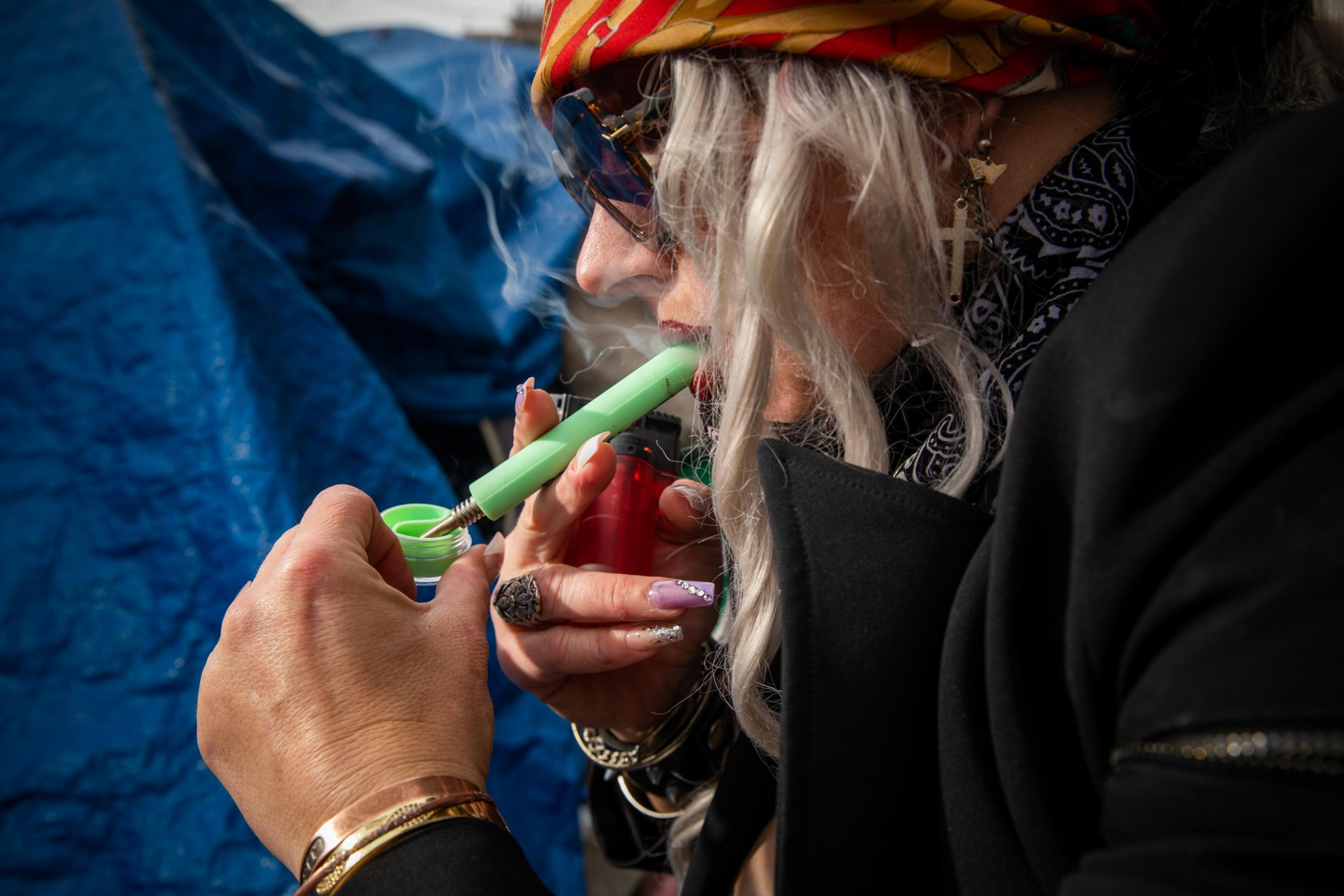A person is lighting a handheld device that emits smoke, with a blue tarp backdrop.