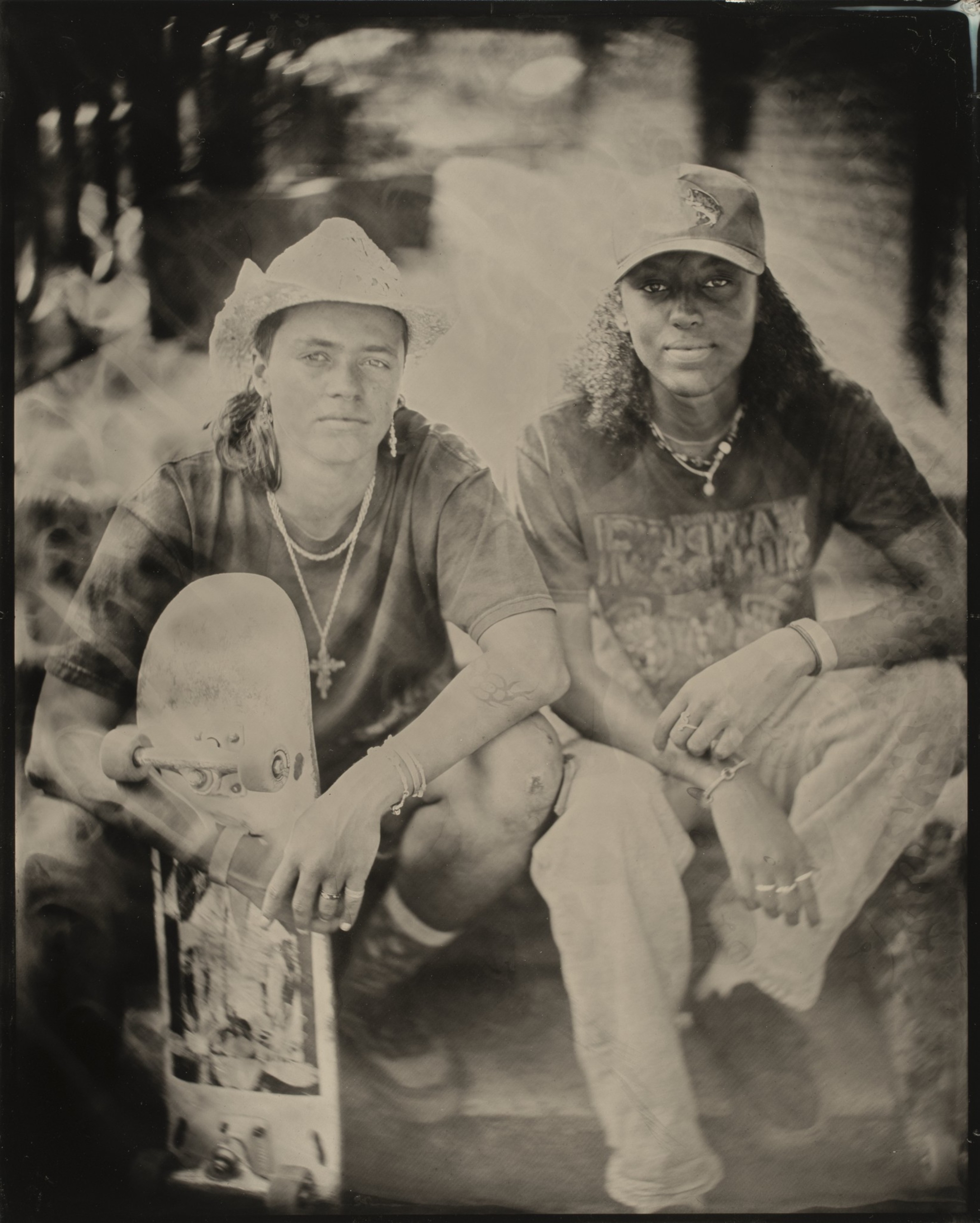 Two individuals are sitting close together; one wears a cowboy hat and holds a skateboard, while the other sports a cap. The image has a vintage, sepia tone.