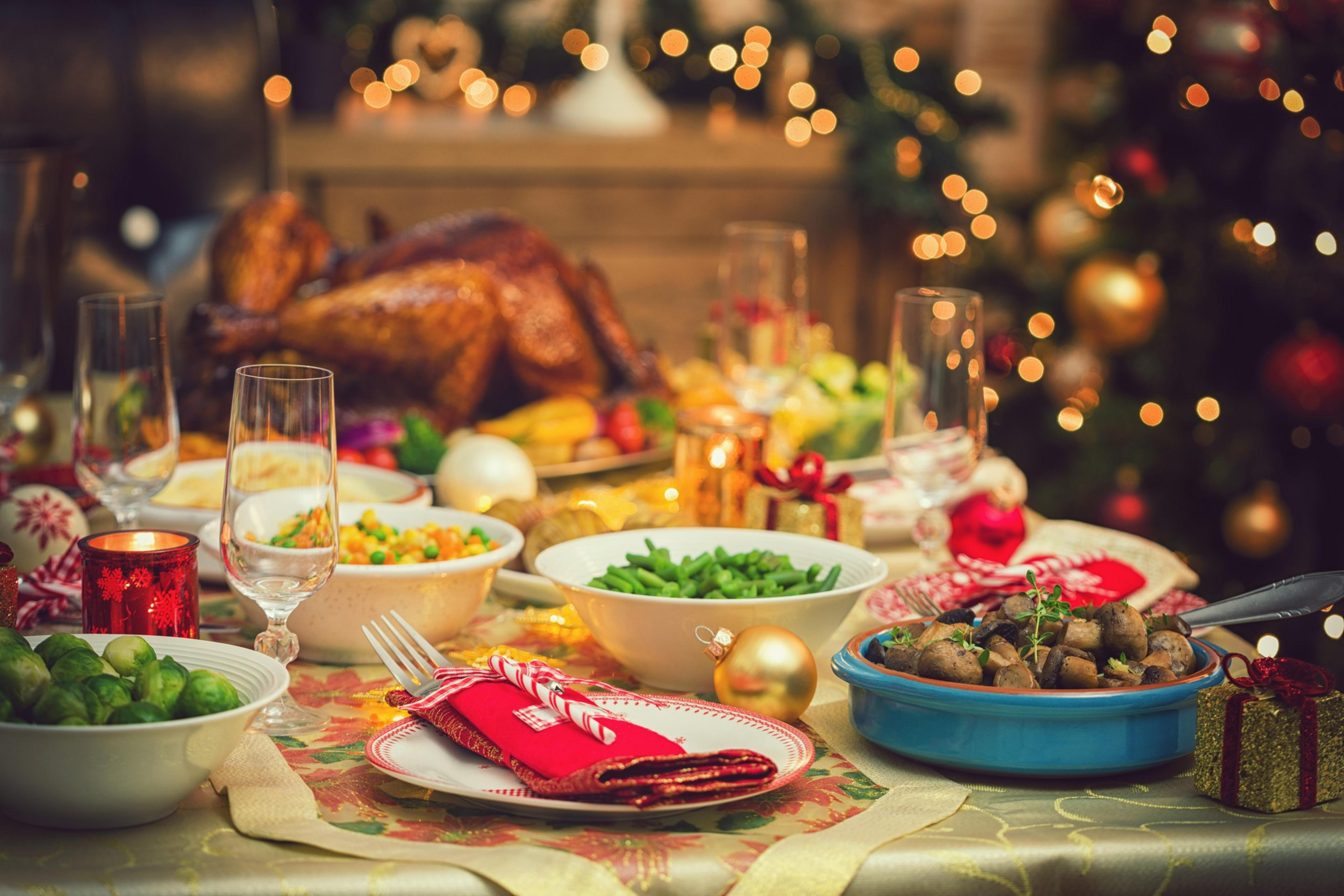 Table is set up for Christmas dinner. On the table is a traditional stuffed roasted turkey with side dishes and Christmas decoration.