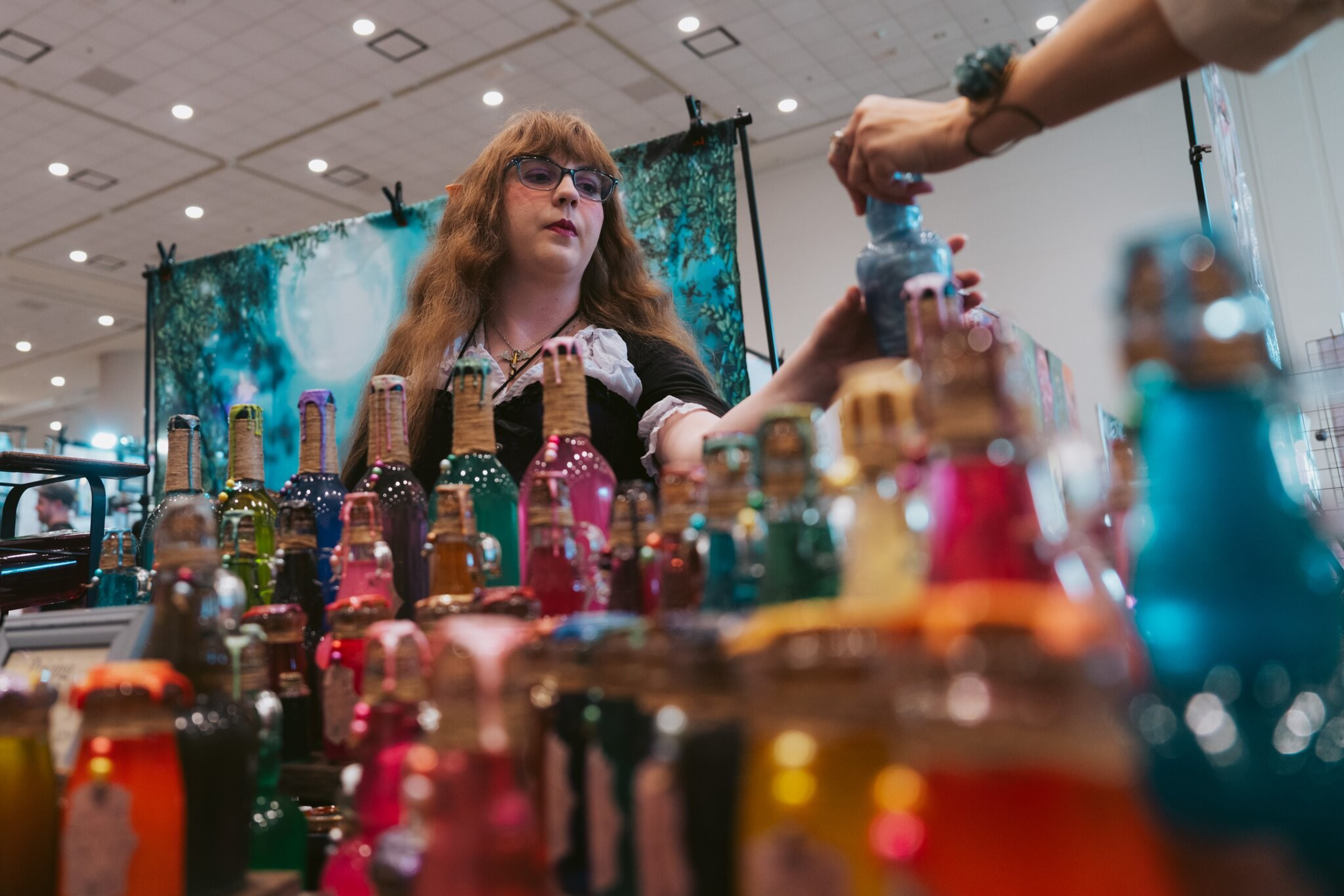 A woman pours cocktails behind an array of colorful glassware.